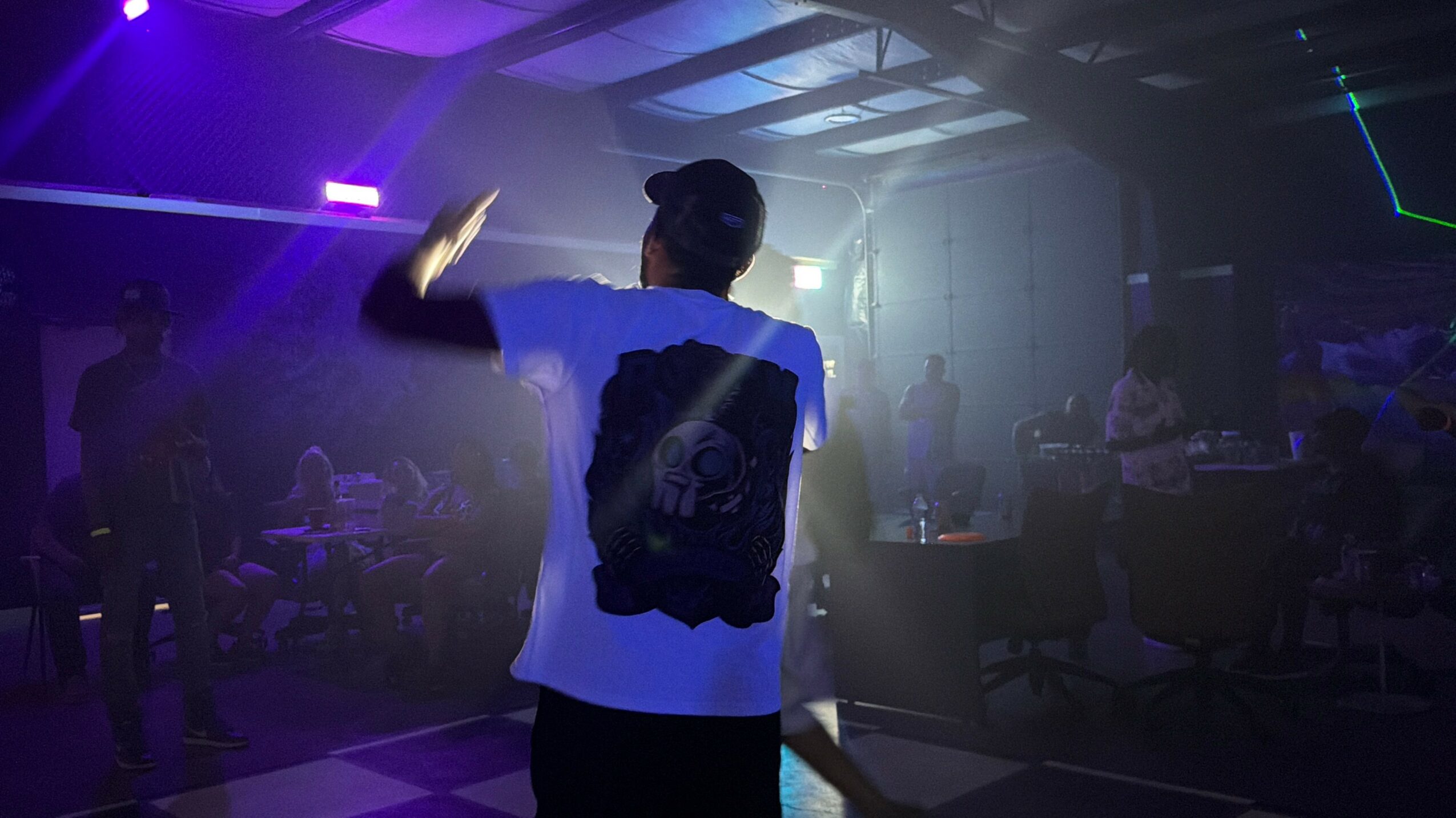 Person dancing in a dimly lit nightclub with colorful lights and other people in the background.