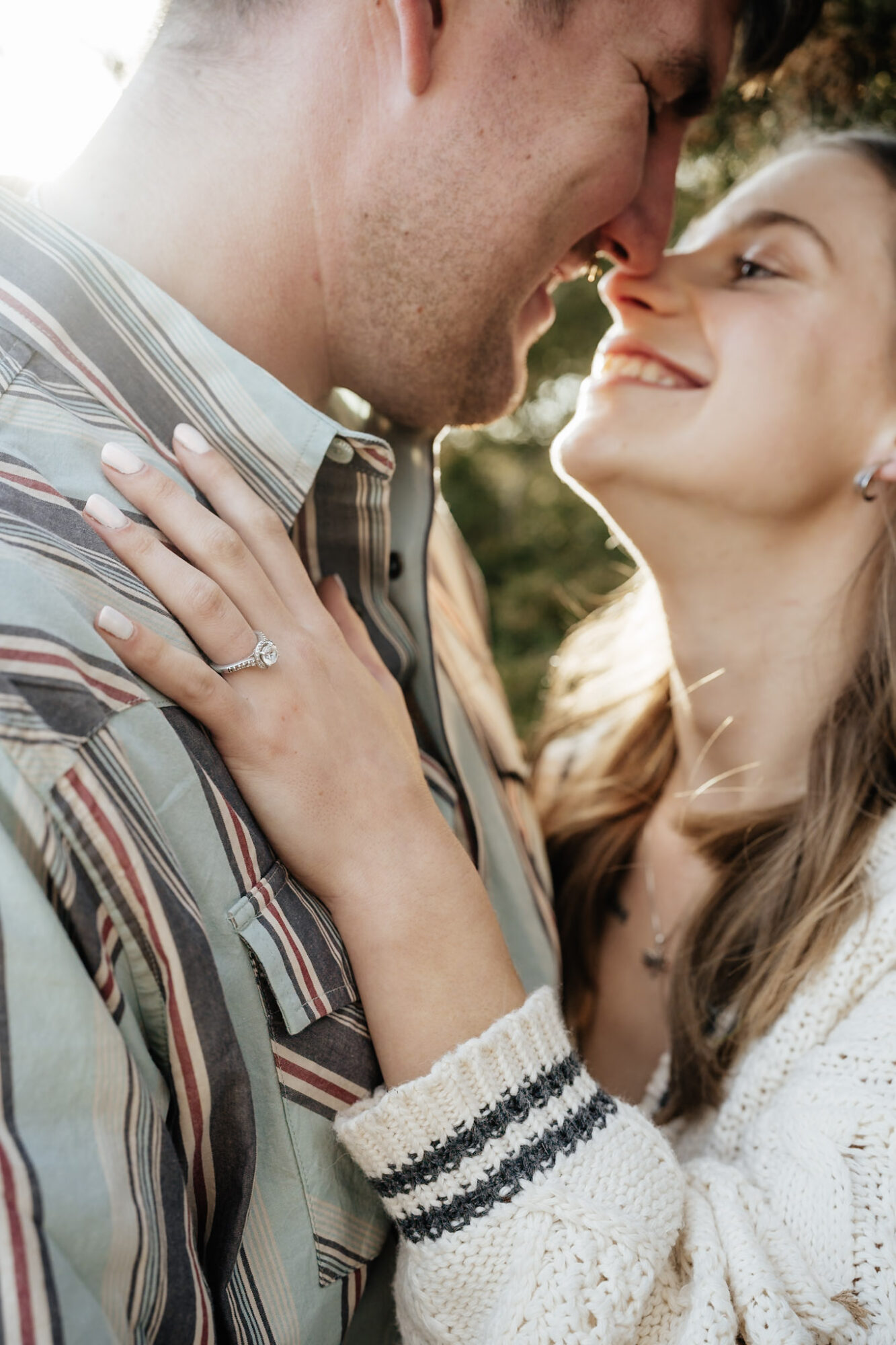 A couple smiling closely outdoors, woman with hand on man's chest, both looking at each other affectionately.