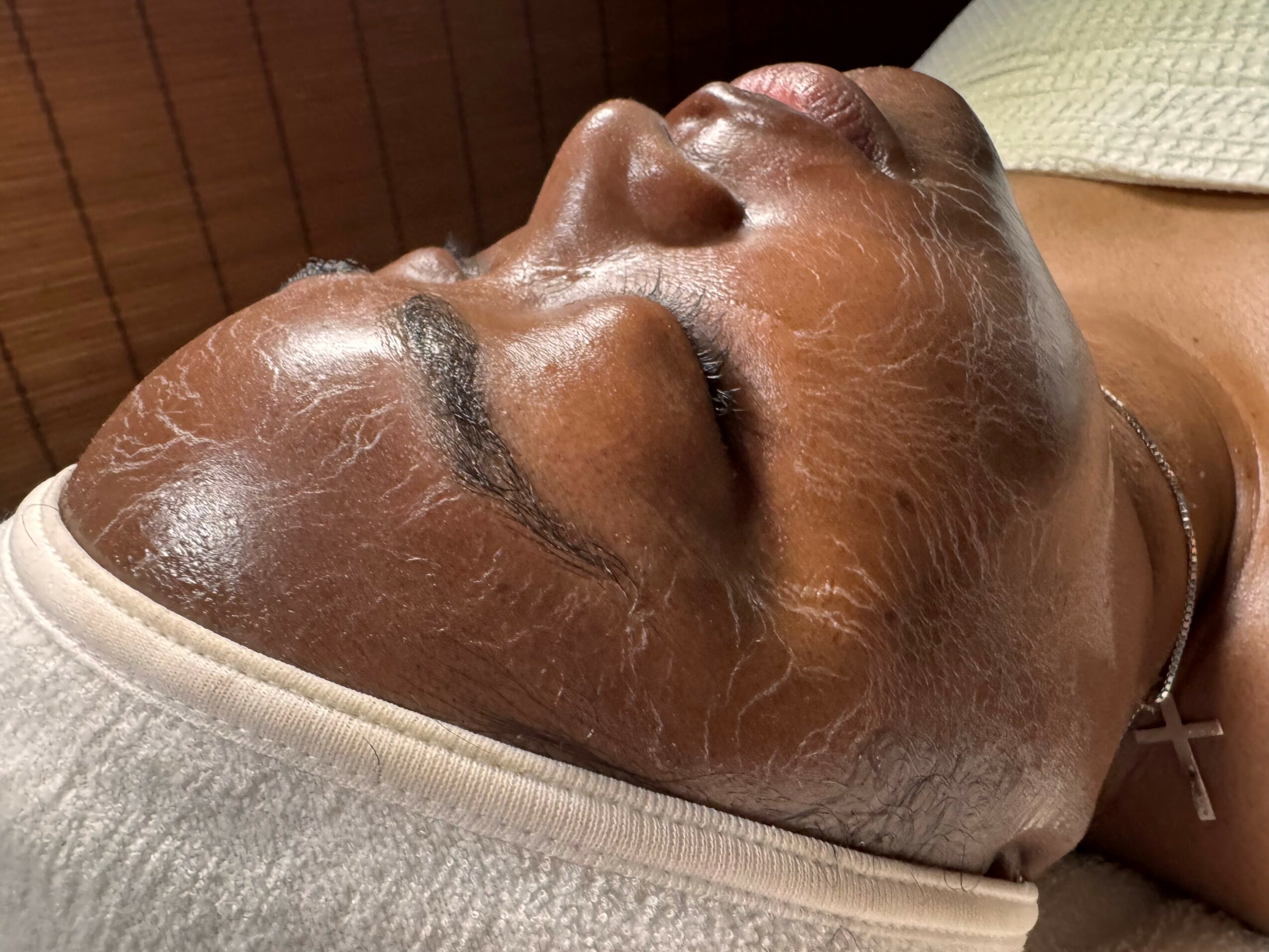 Person lying down with a facial mask, eyes closed, wearing a headband, in a spa or skincare setting.