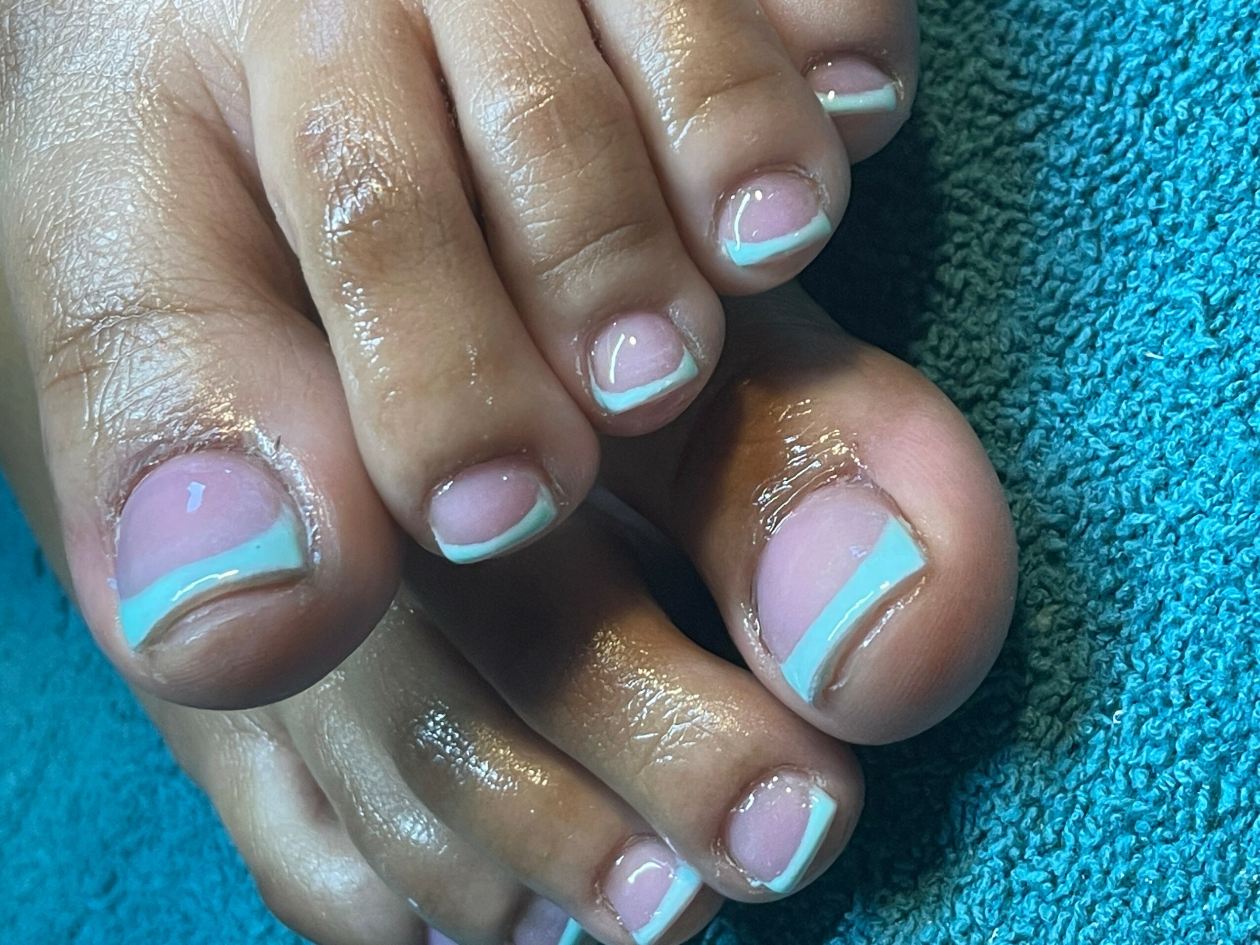 Close-up of toes with painted nails, resting on a blue towel, showing skin and nail details.