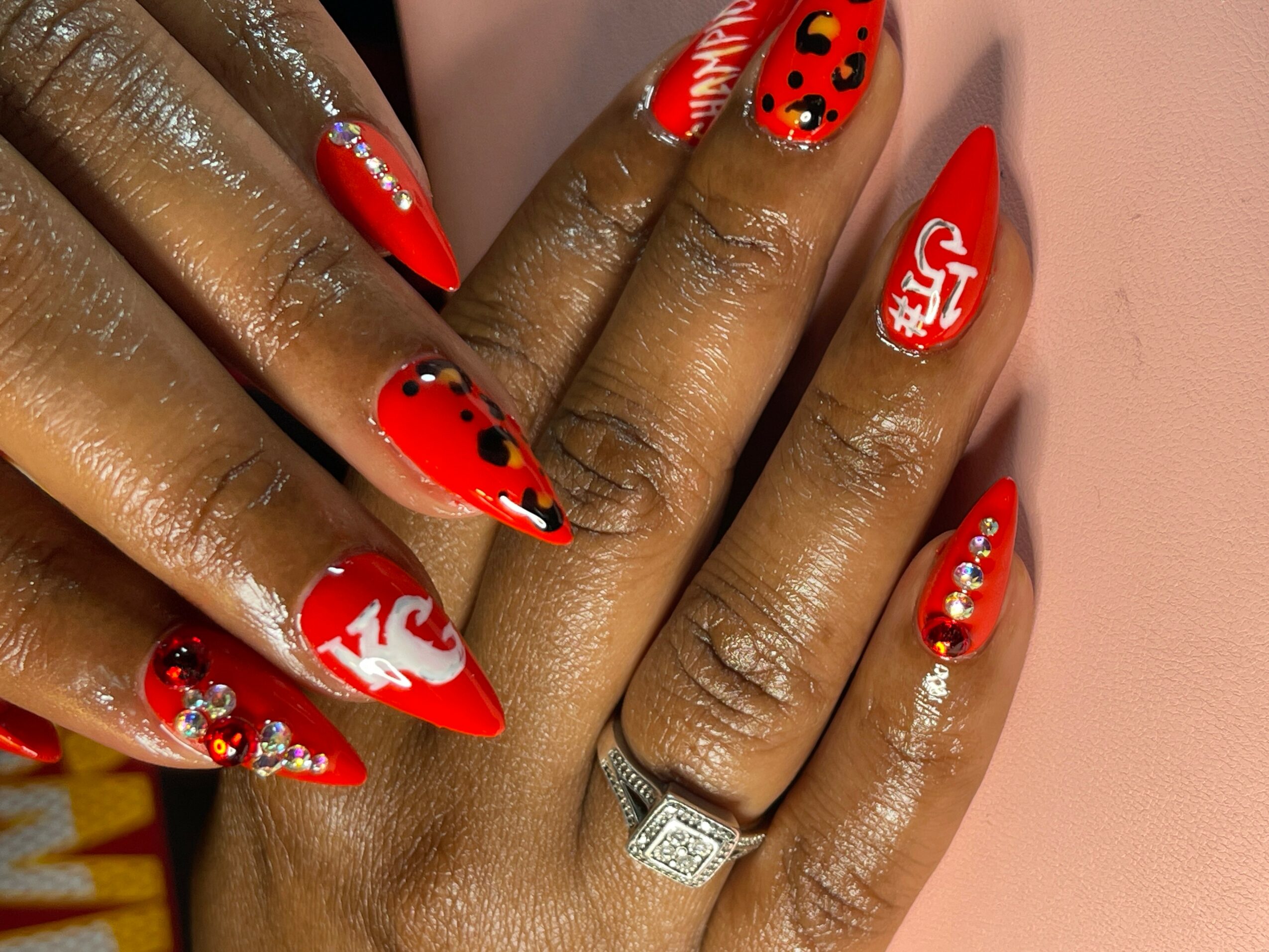 Close-up of hands with red and white nail art, decorated with rhinestones and black dots, and a ring on one finger.