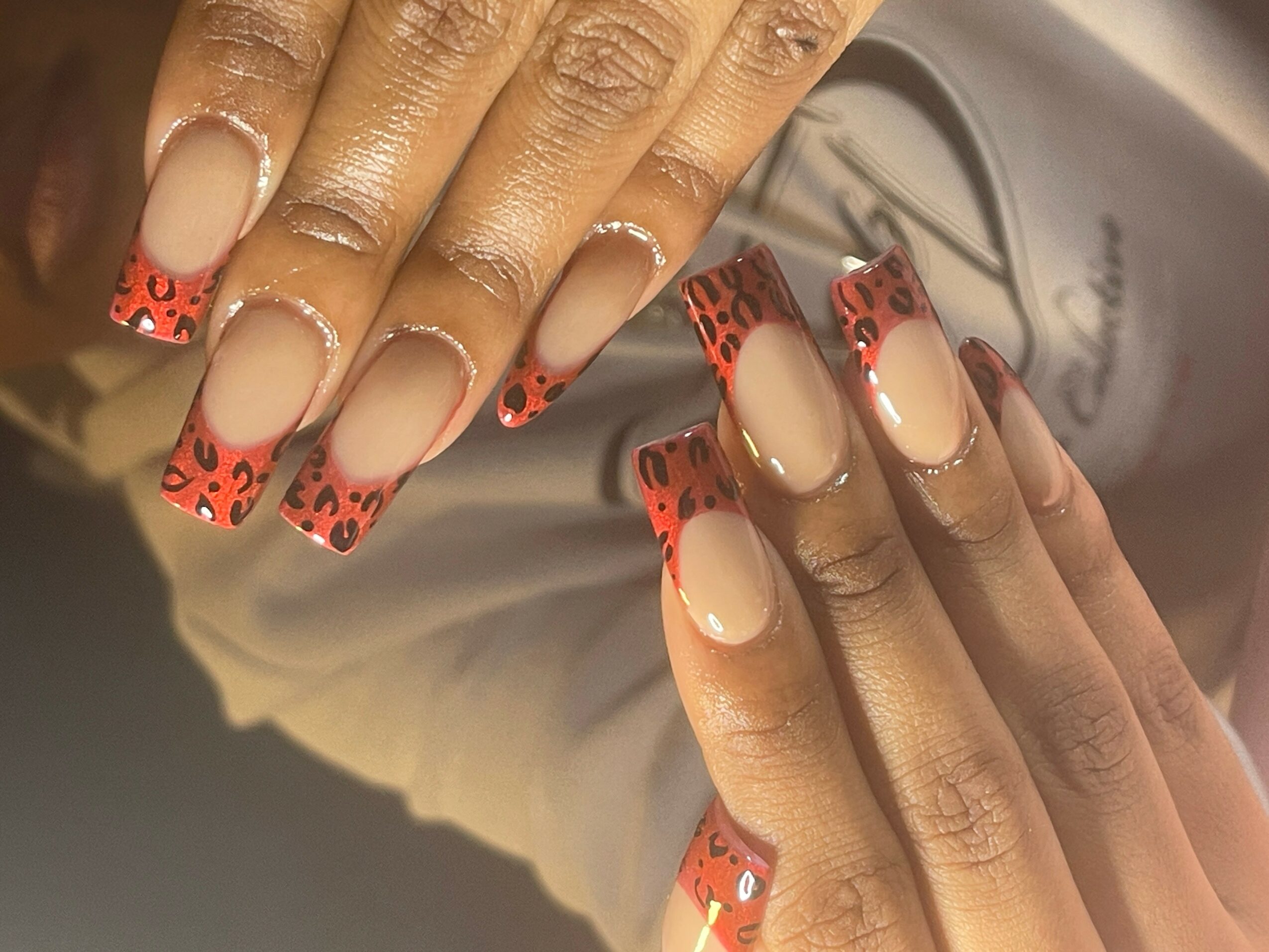 Close-up of hands with decorated nails featuring a beige base and red leopard print tips.