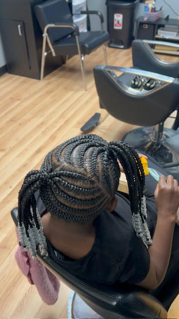 Person with braided hair sitting in a chair in a room with chairs and a wooden floor.