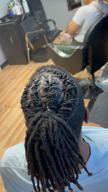 Top view of a person with neatly styled dreadlocks, sitting in a room with a person in the background.