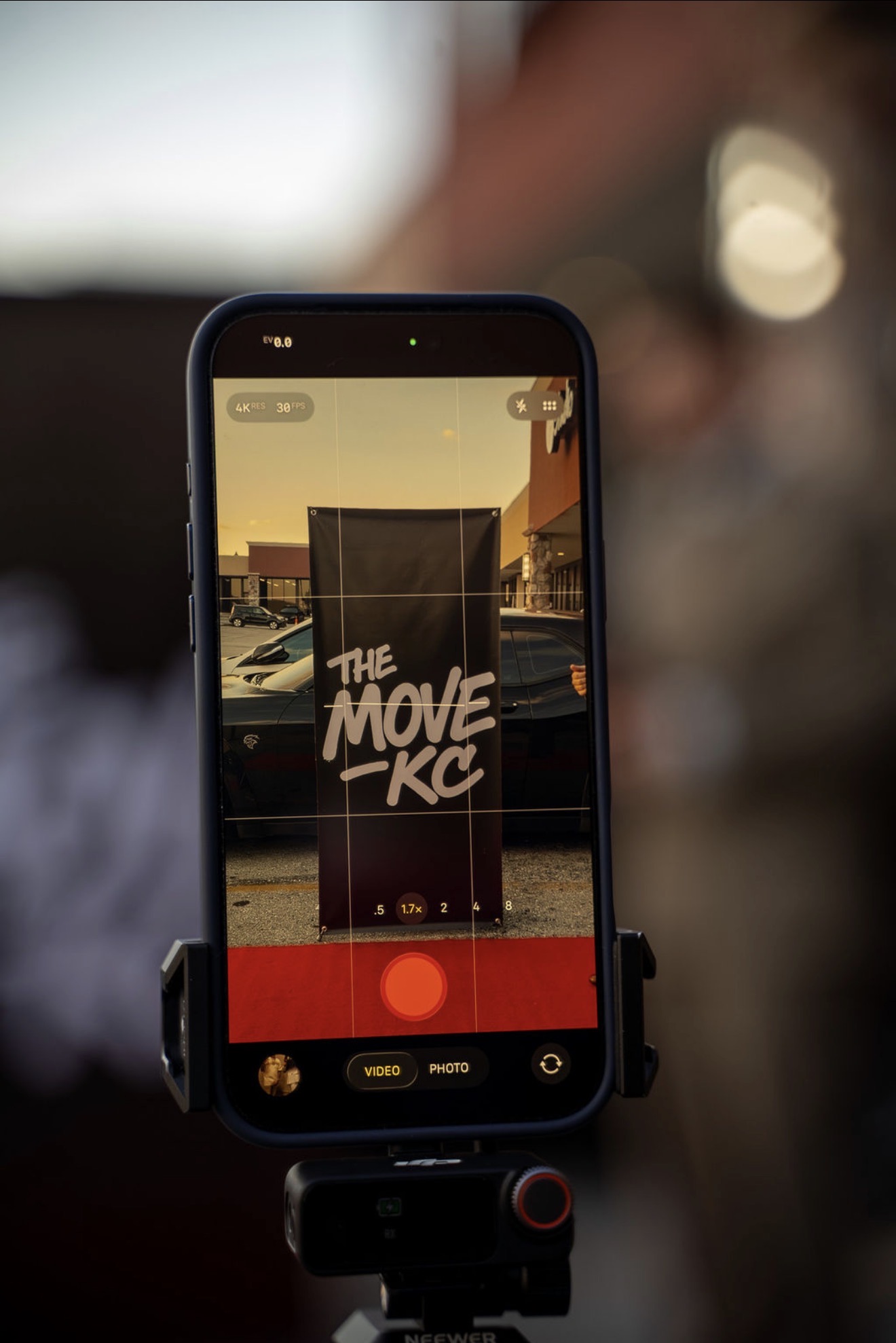 Smartphone on a tripod recording a sign that reads 'The Move Kick' outdoors during sunset.