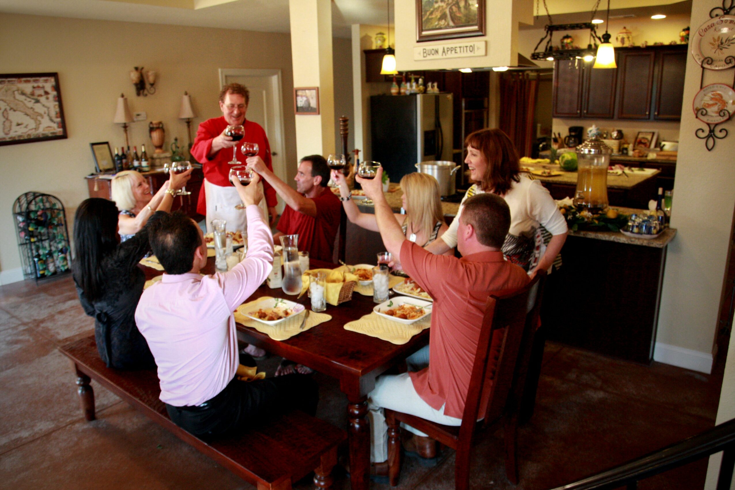 Group of people celebrating around a dining table with food, raising glasses in a restaurant or cafe setting.