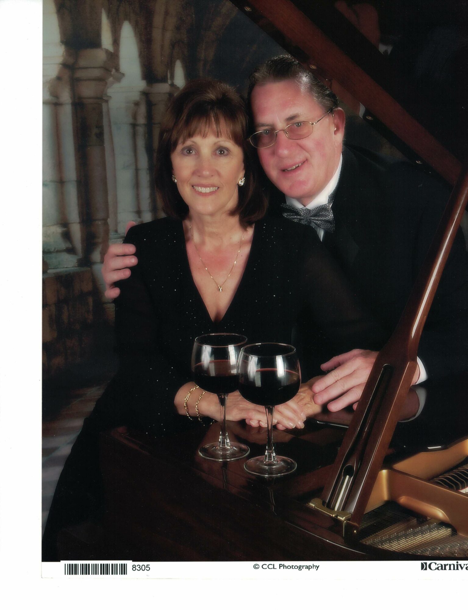 Two people, a woman and a man, sit at a table with two glasses of red wine, smiling, in an elegant setting.