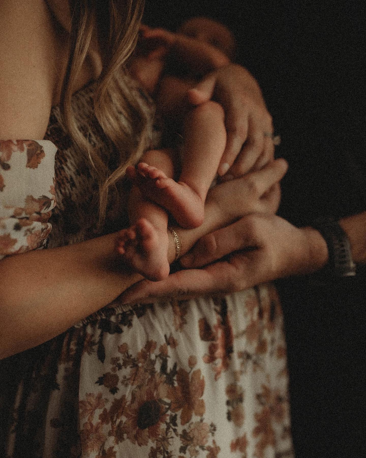 Person holding a newborn baby with adult hands supporting the baby, wearing a floral dress.