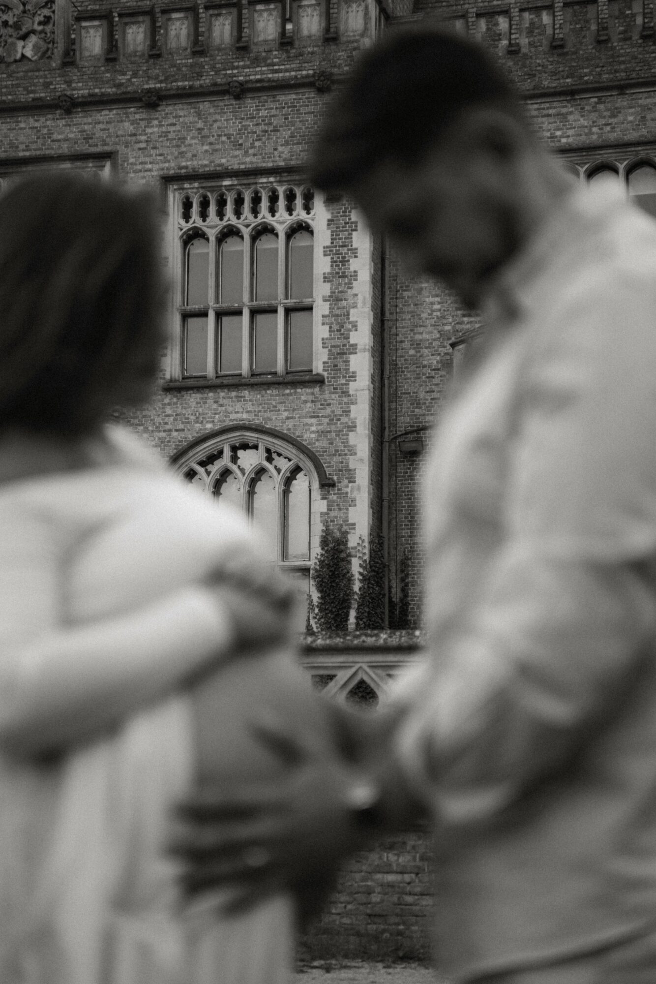 Two people standing outdoors in front of a historic building with arched windows, one person appears pregnant.