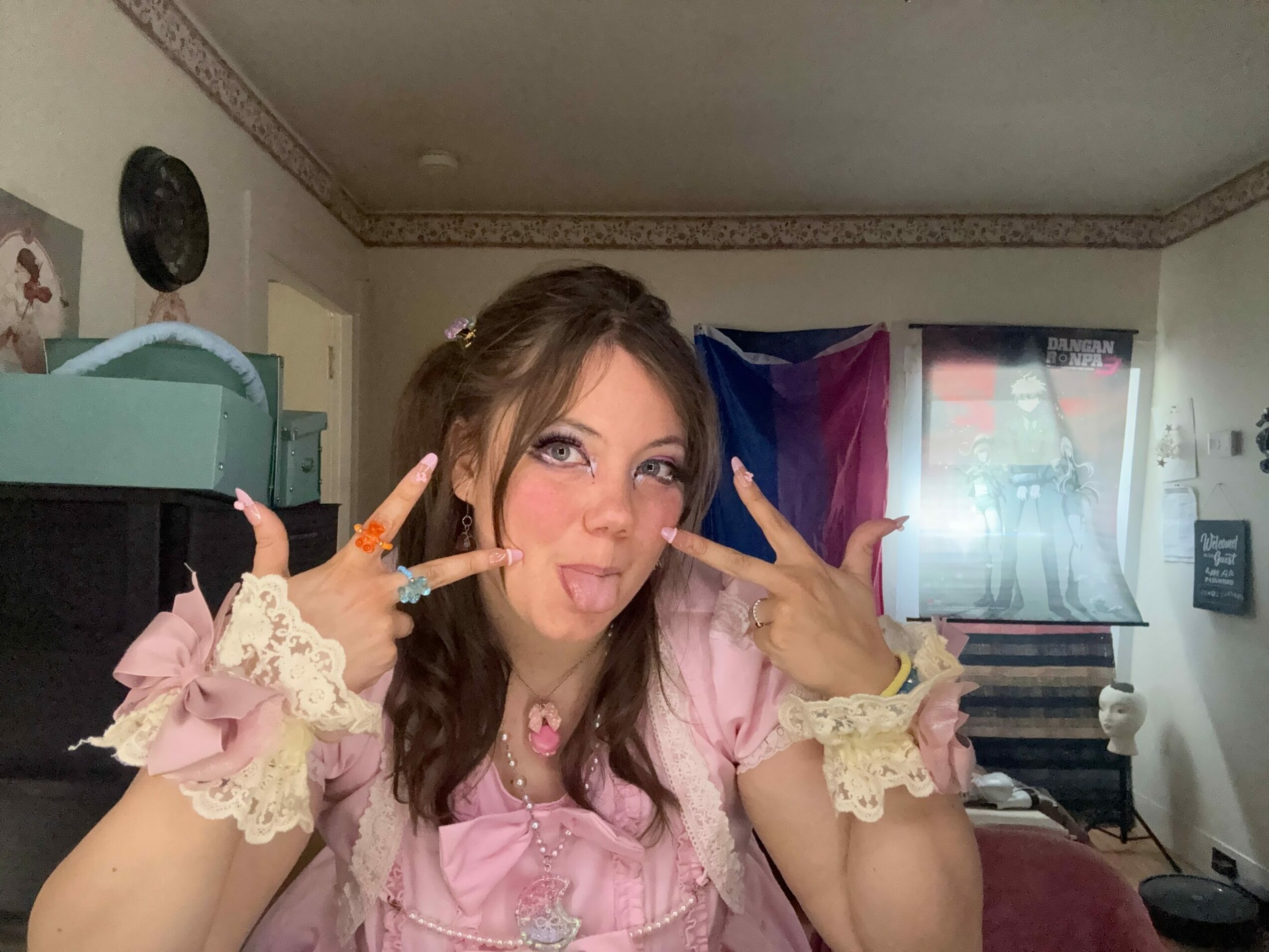 Young woman with long brown hair in pink dress making peace signs, smiling, indoors.
