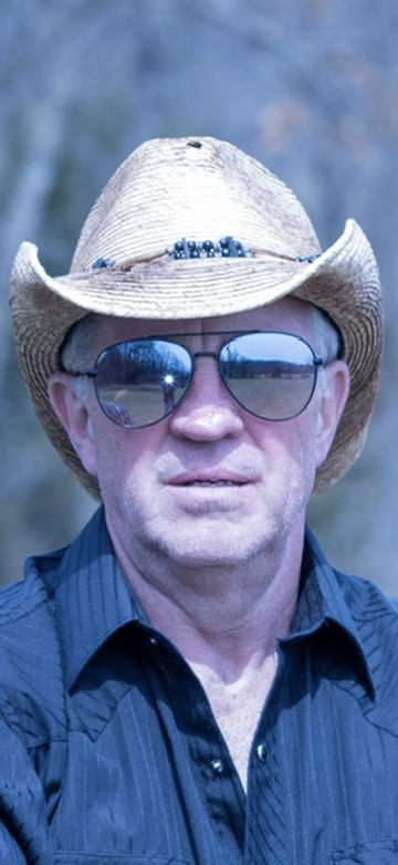 Man wearing a straw hat and sunglasses outdoors, with a blurred natural background.