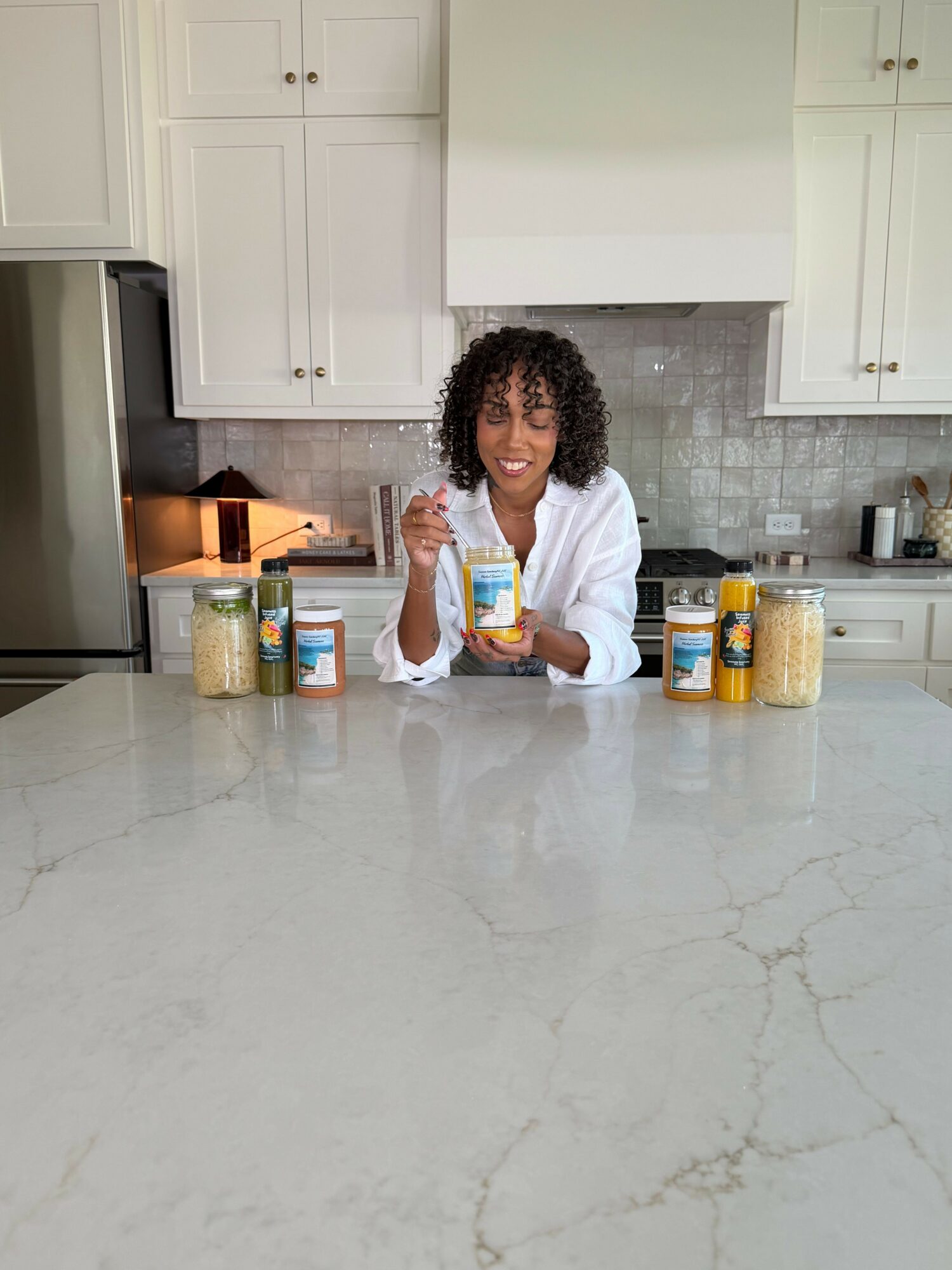 Woman with curly hair in a white shirt arranging bottles on a kitchen counter.