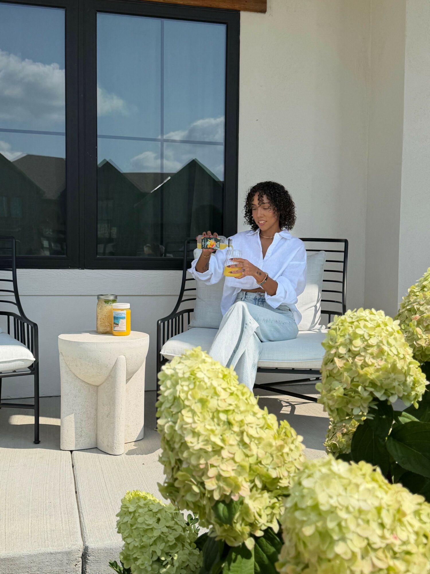 Person sitting on a chair on a balcony, holding a drink, with large white flowers in foreground.