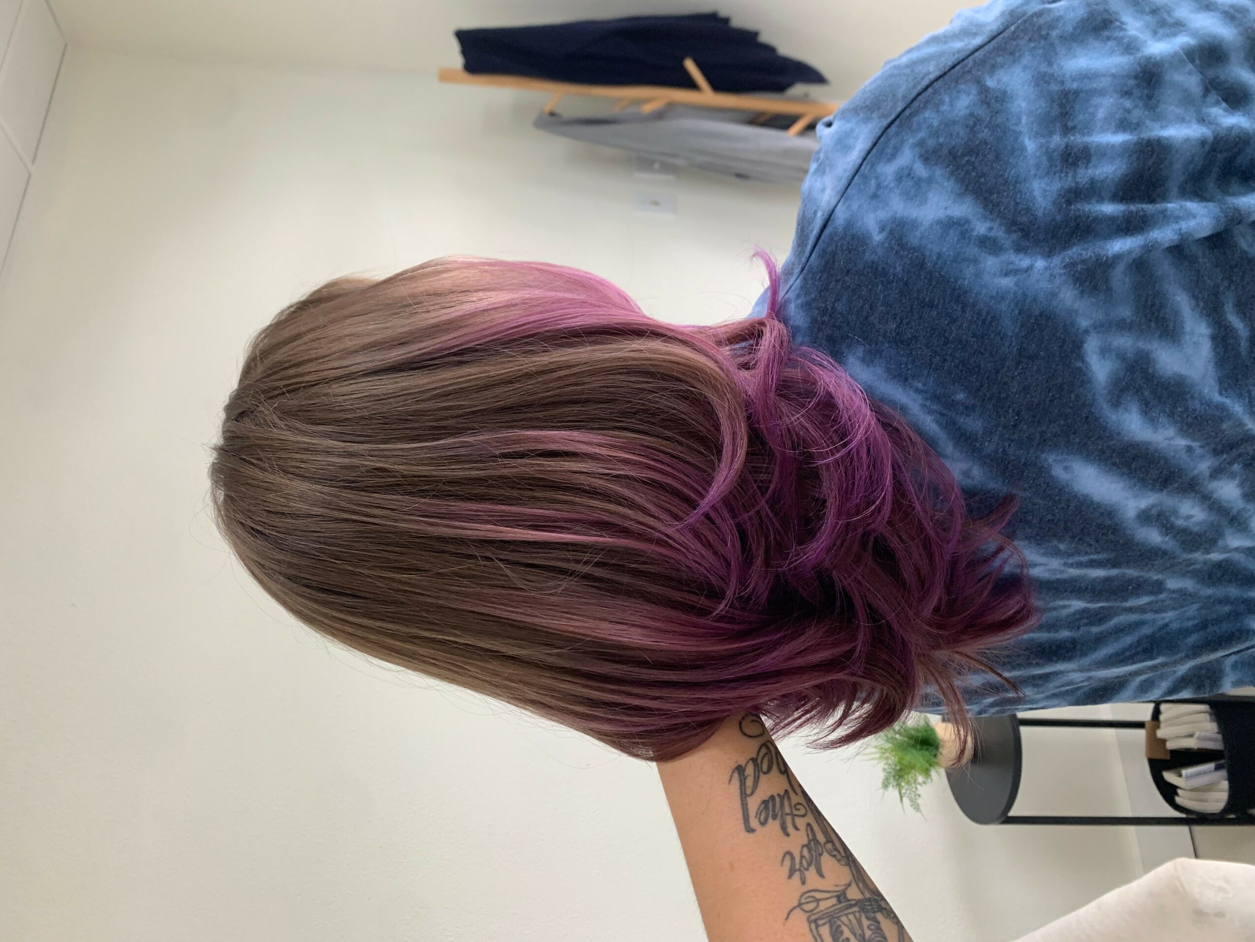 Person with shoulder-length hair dyed pink and purple, wearing a blue denim jacket, facing away from the camera.