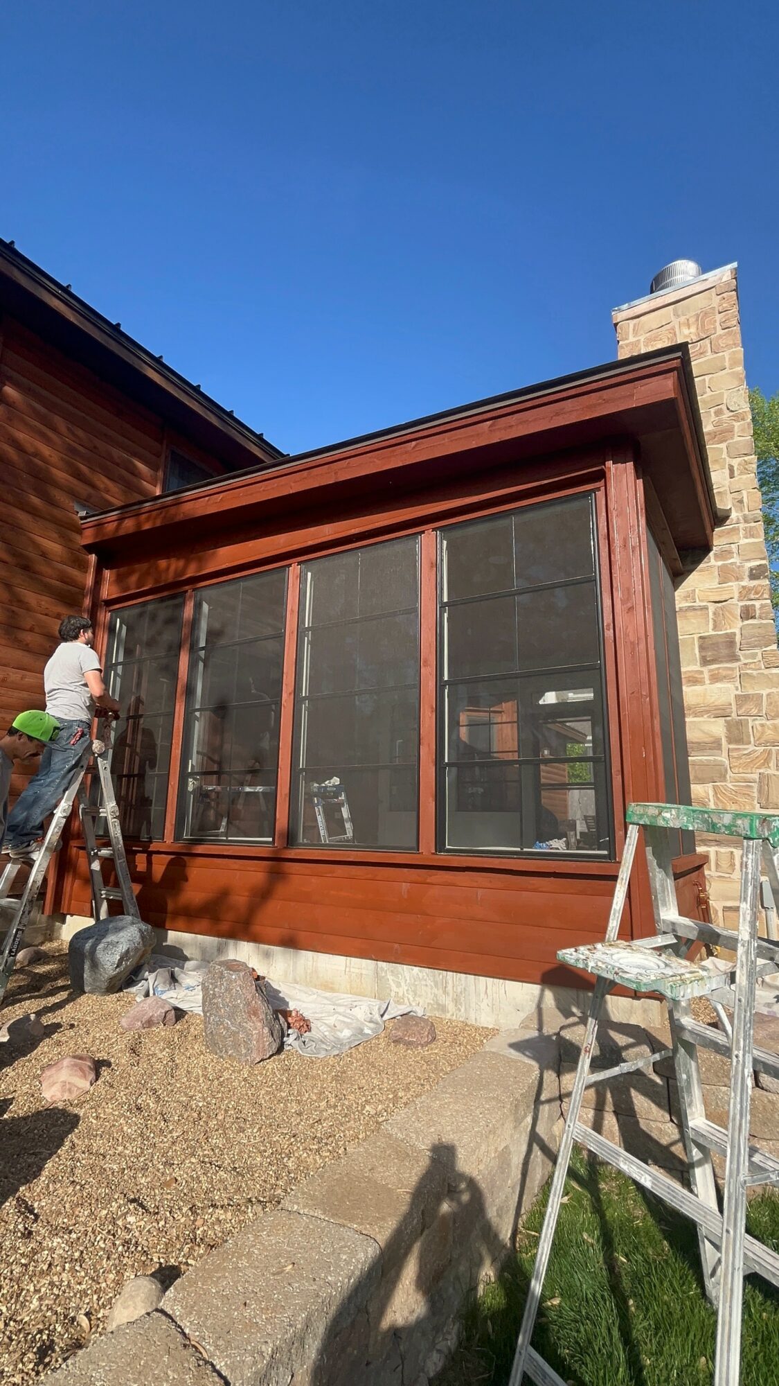 Construction site with a screened porch attached to a house, blue sky, and construction tools nearby.