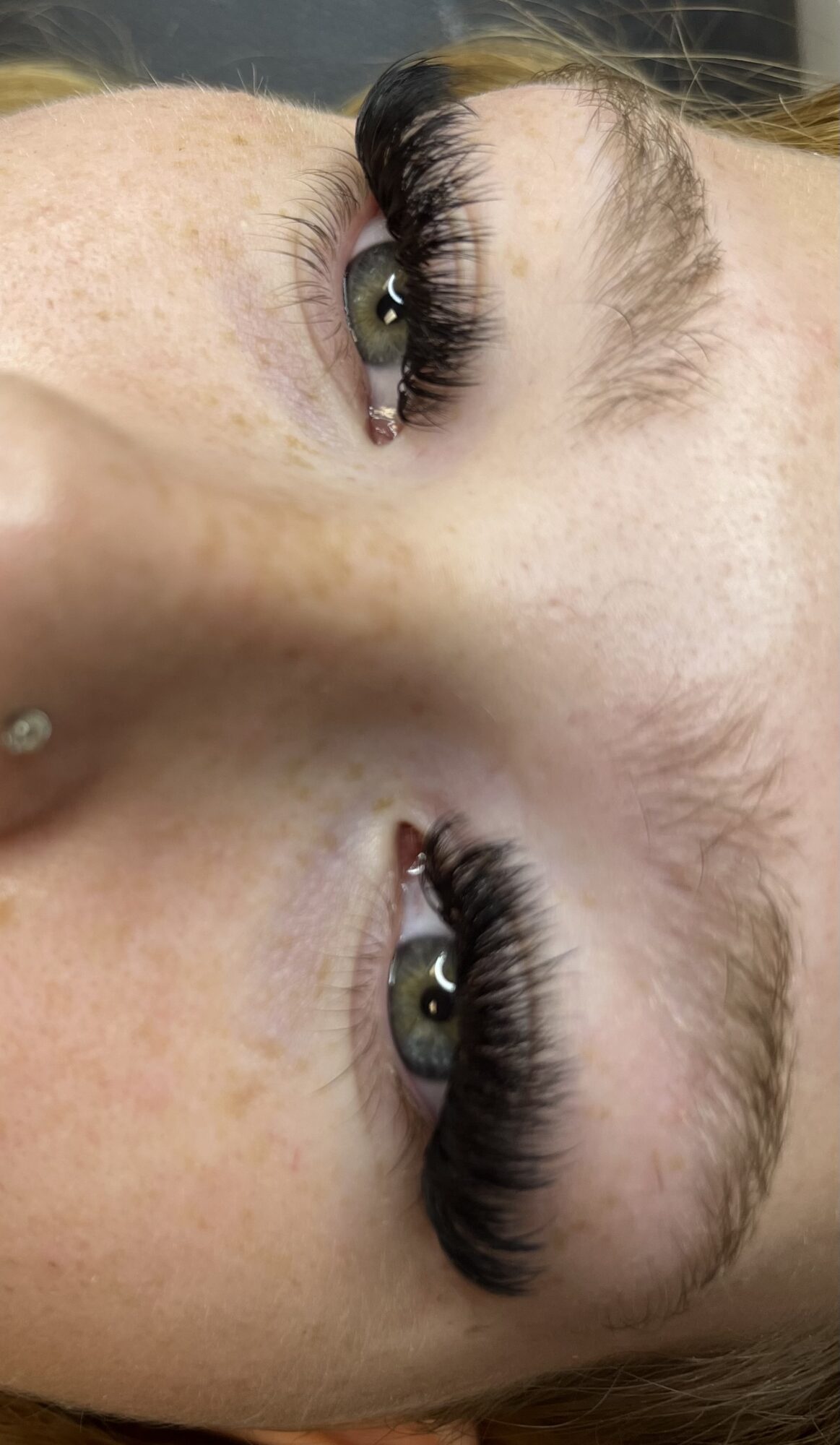 Close-up of a person's eyes with long eyelashes, lying sideways, with visible eyebrows and skin texture.
