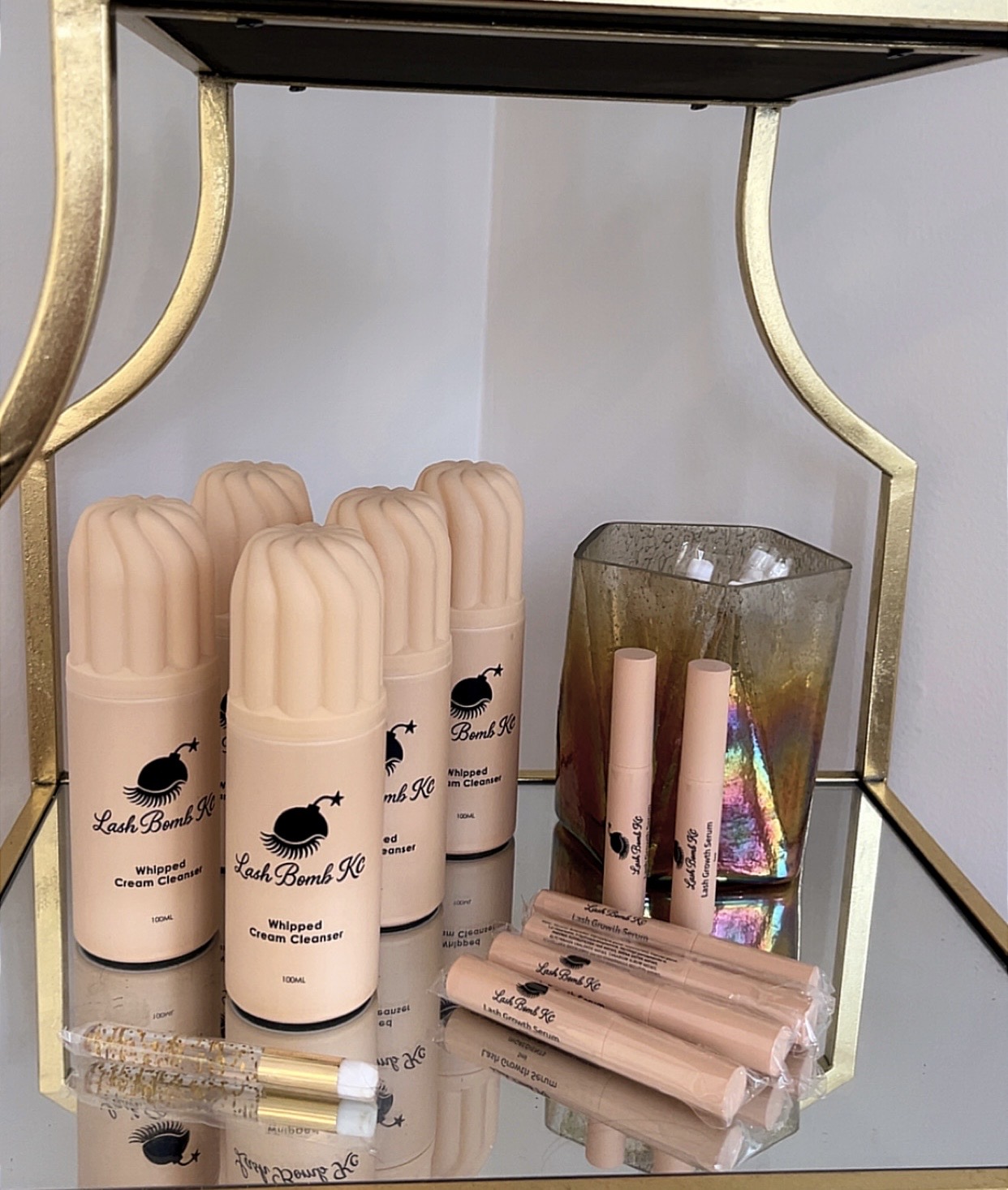 Four beige cylindrical containers with black whale logo, a glass with rolled paper, and small wrapped items on a glass shelf.