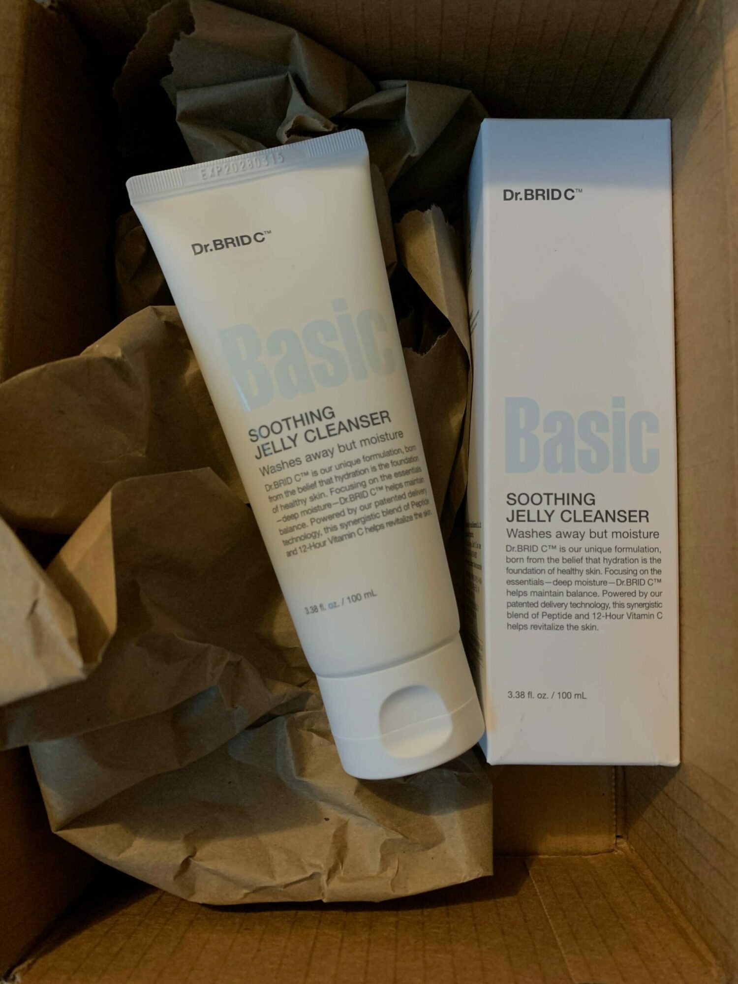 A white bottle and box inside a cardboard box with crumpled paper, labeled 'Basic' and 'Dermo' for skincare.