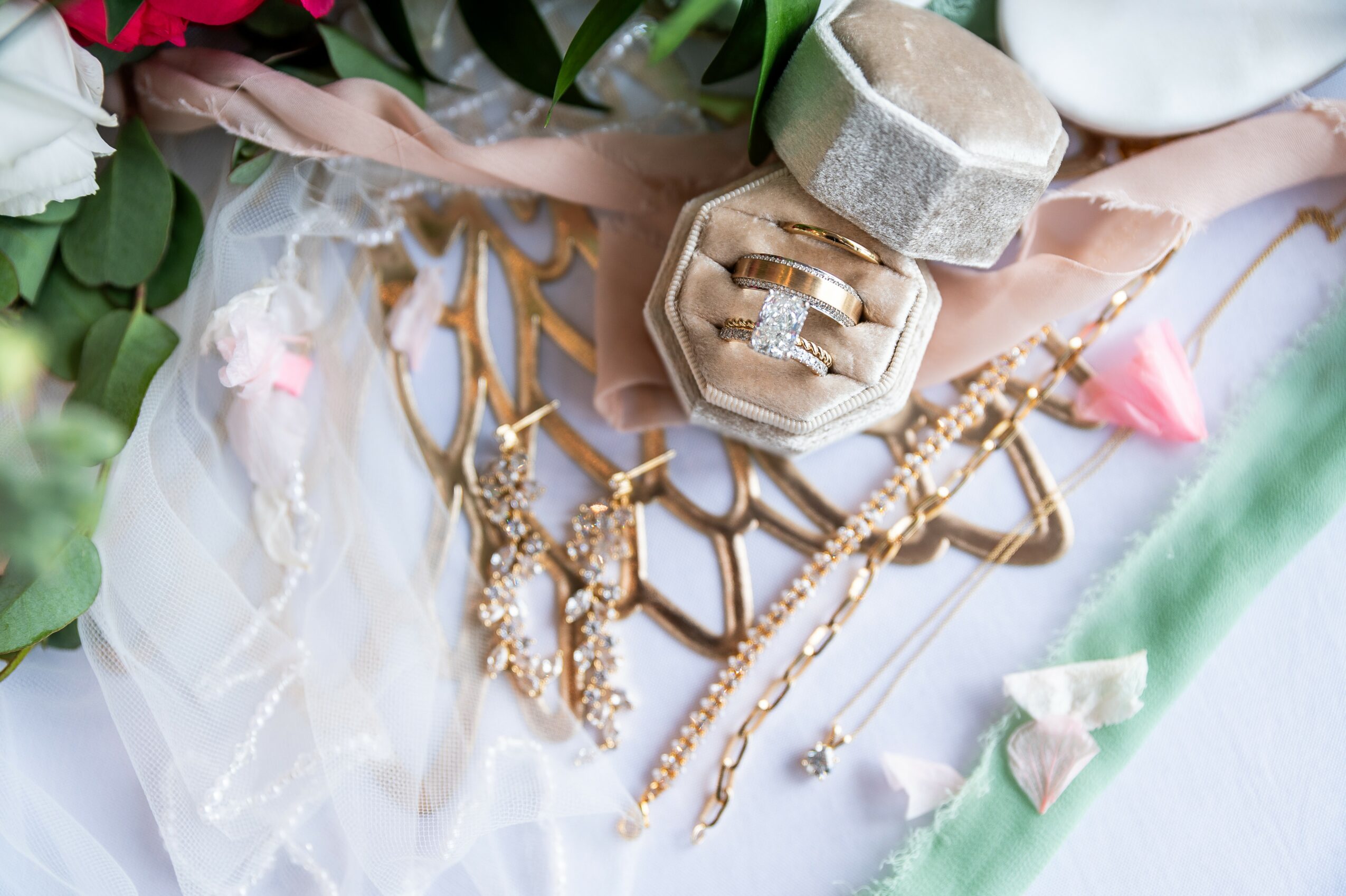 Jewelry including necklaces, rings, and earrings arranged on fabric with flowers and decorative items.