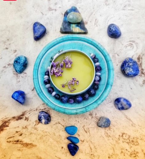 A yellow candle surrounded by blue beads, with blue and green stones around it on a textured surface.