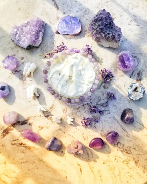 Arrangement of purple and white crystals and stones with a circular shell centerpiece, on a light surface.