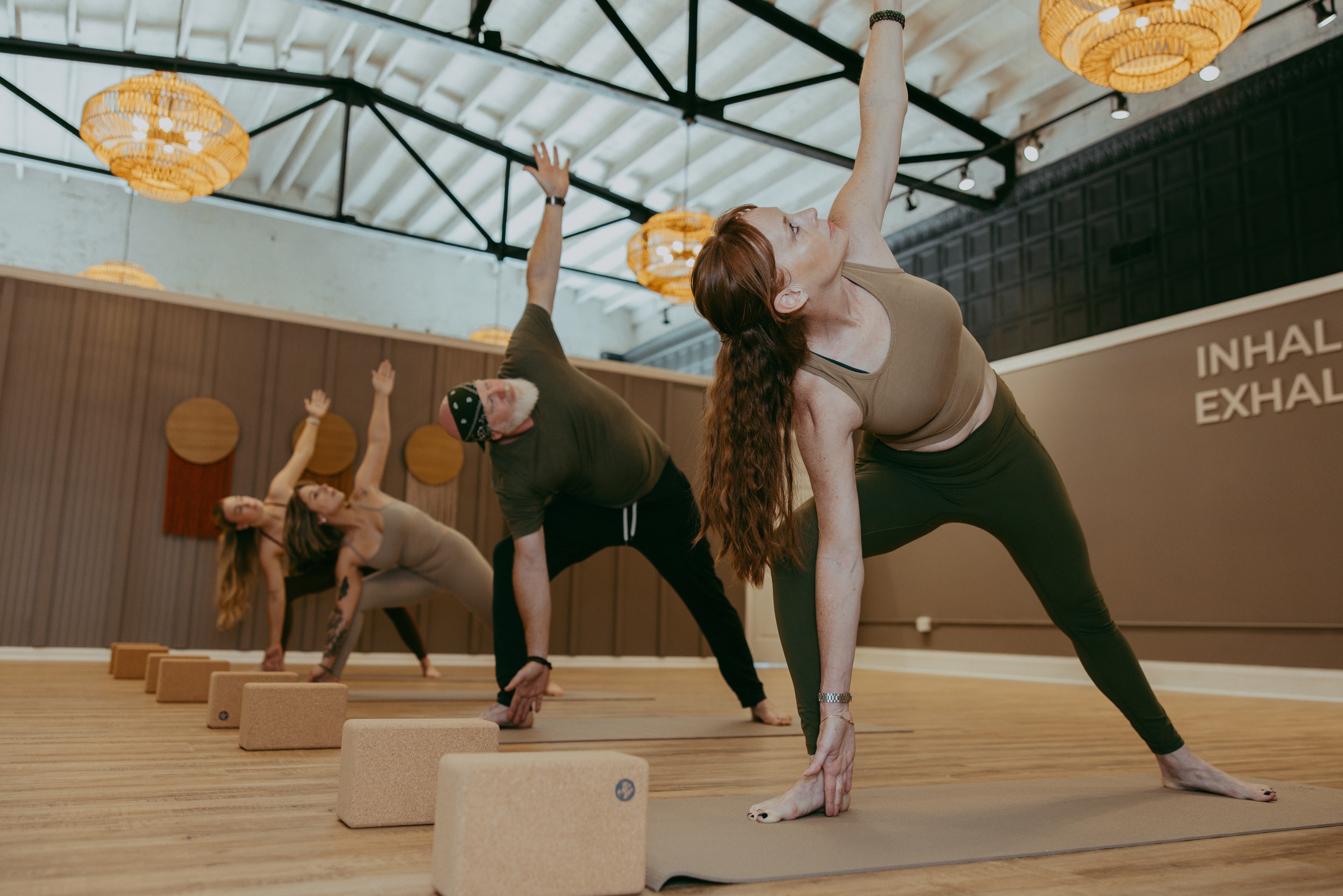 Four people practicing yoga or stretching on blocks in a studio with hanging lights and wooden walls.