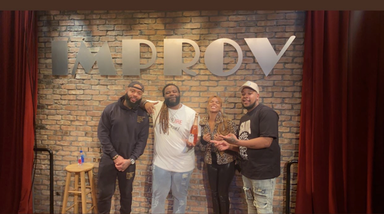 Four people standing on stage in front of a brick wall with large letters spelling 'HAPPY'.