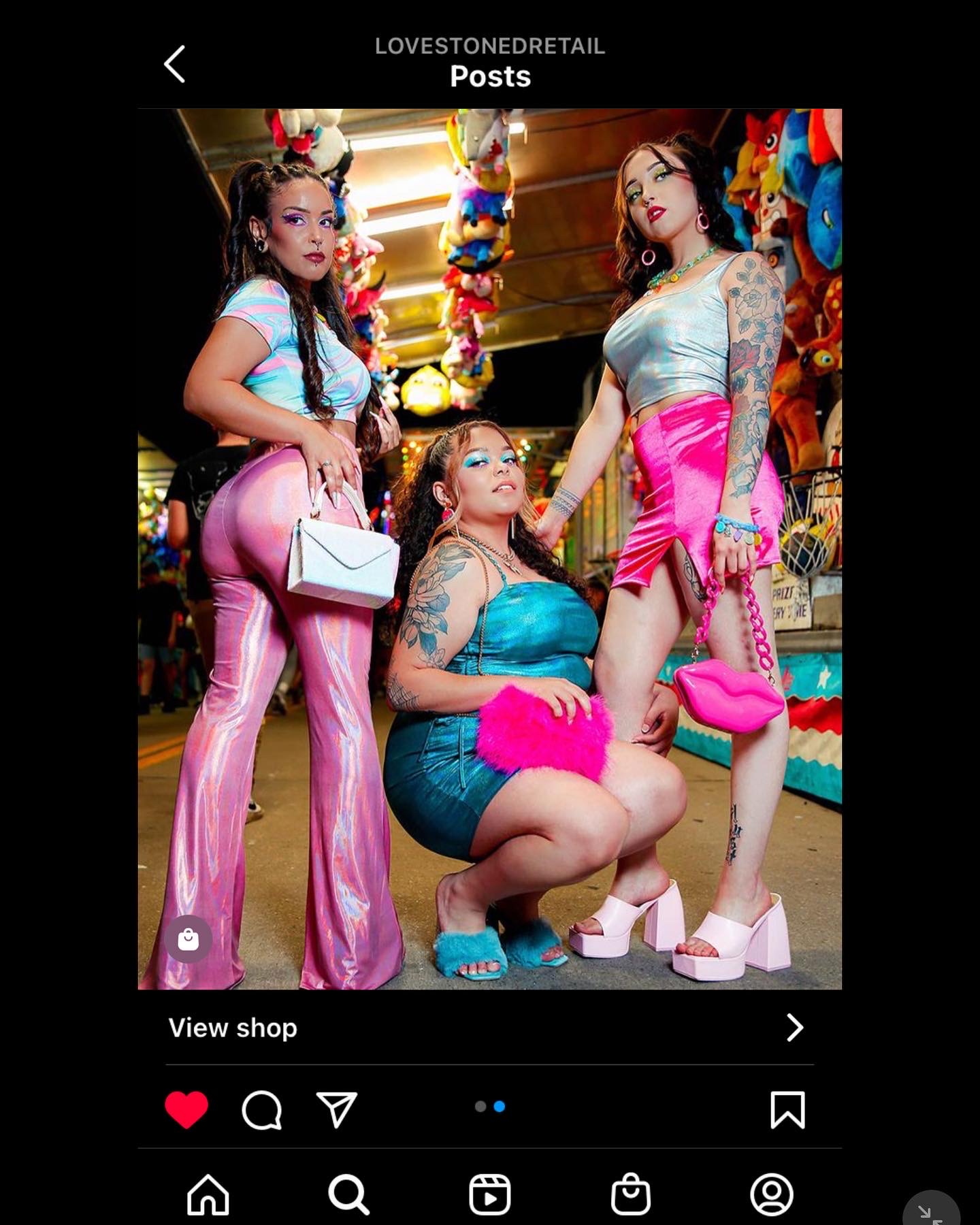 Three women in colorful outfits at a market stall with balloons and toys, posing for a photo.