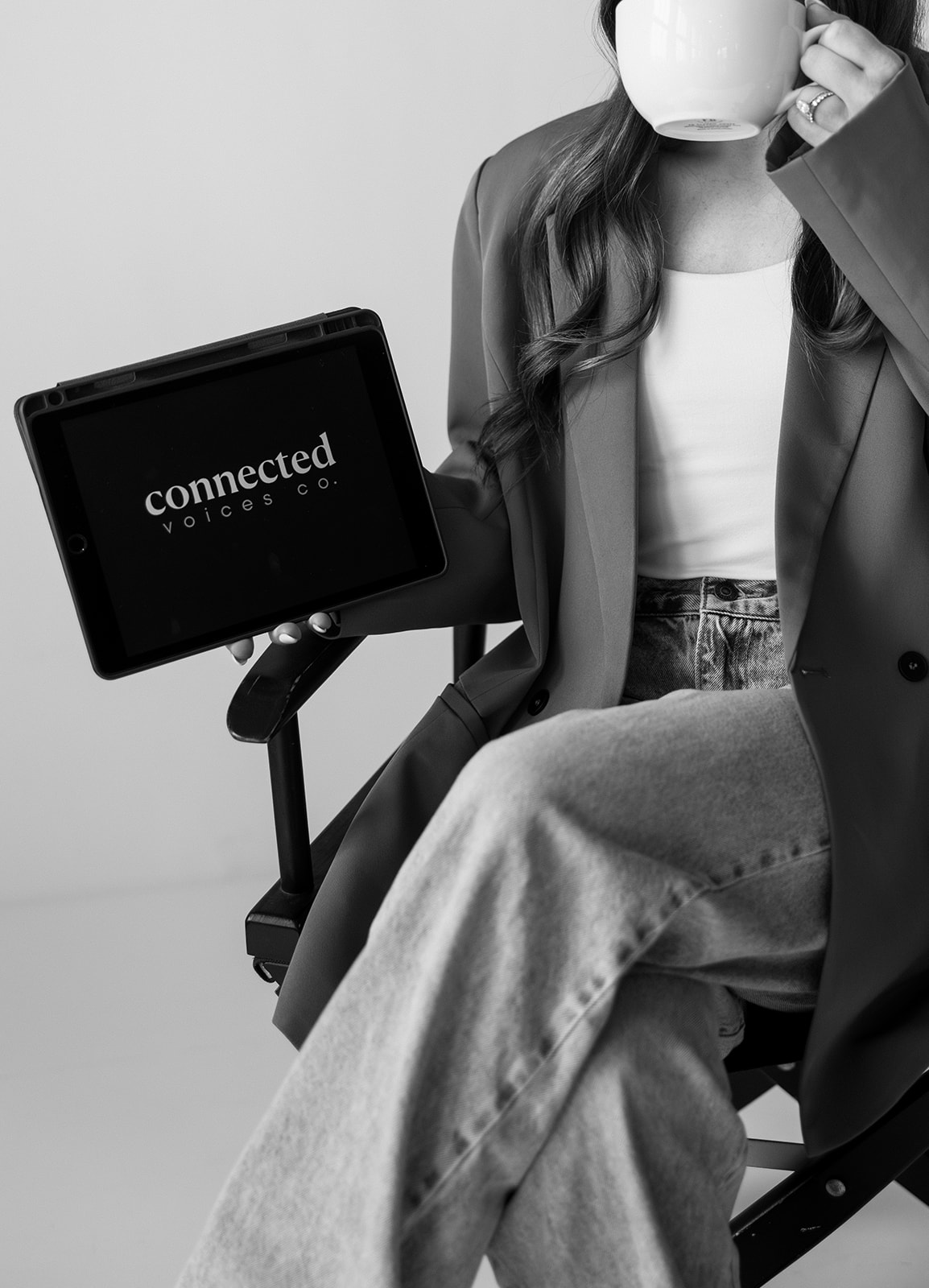Person sitting with crossed legs, holding a mug, and a laptop displaying 'connected' logo, in black and white.