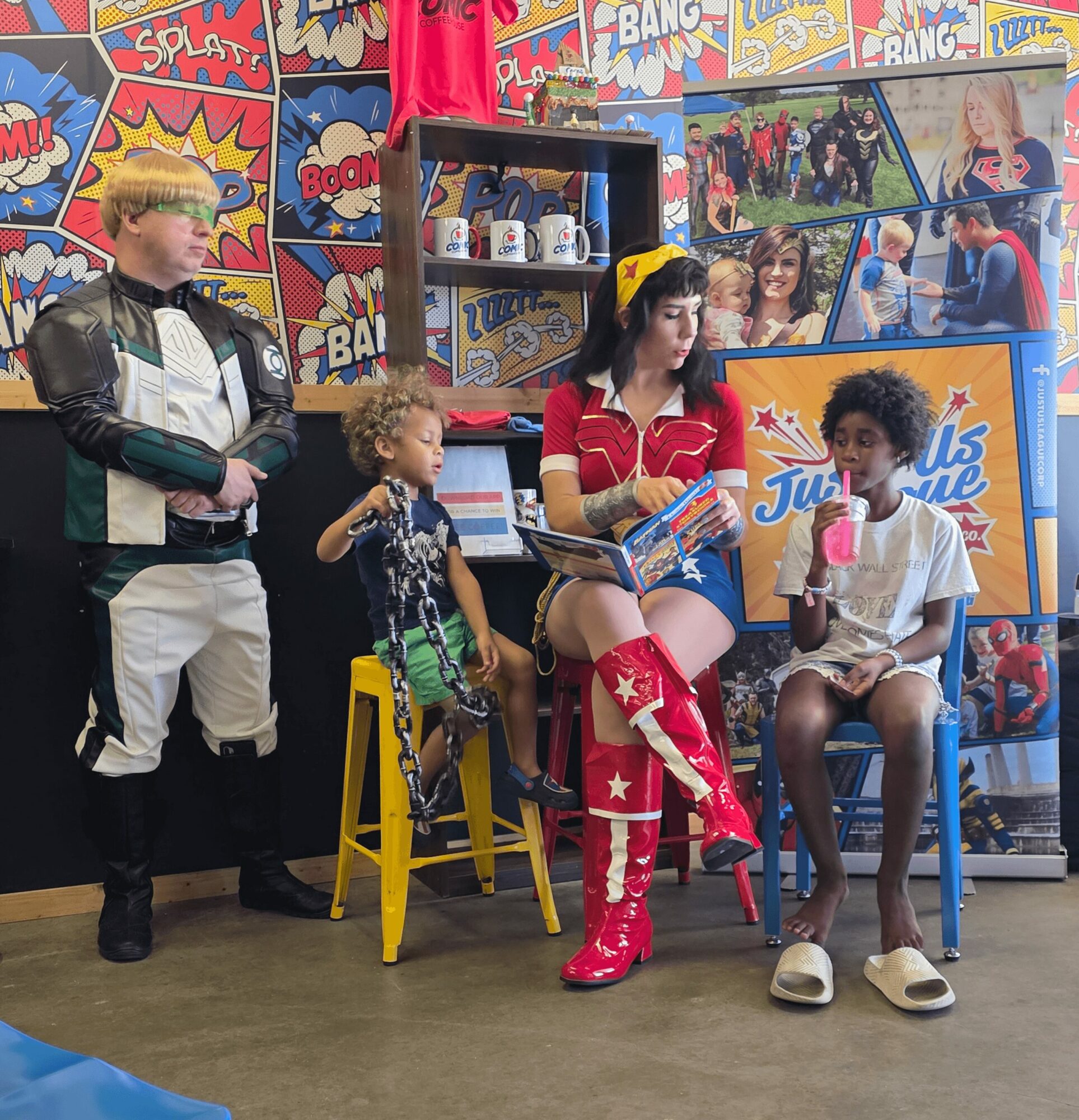 Four people in a colorful comic book-themed room, with two children sitting on chairs and two adults standing nearby.