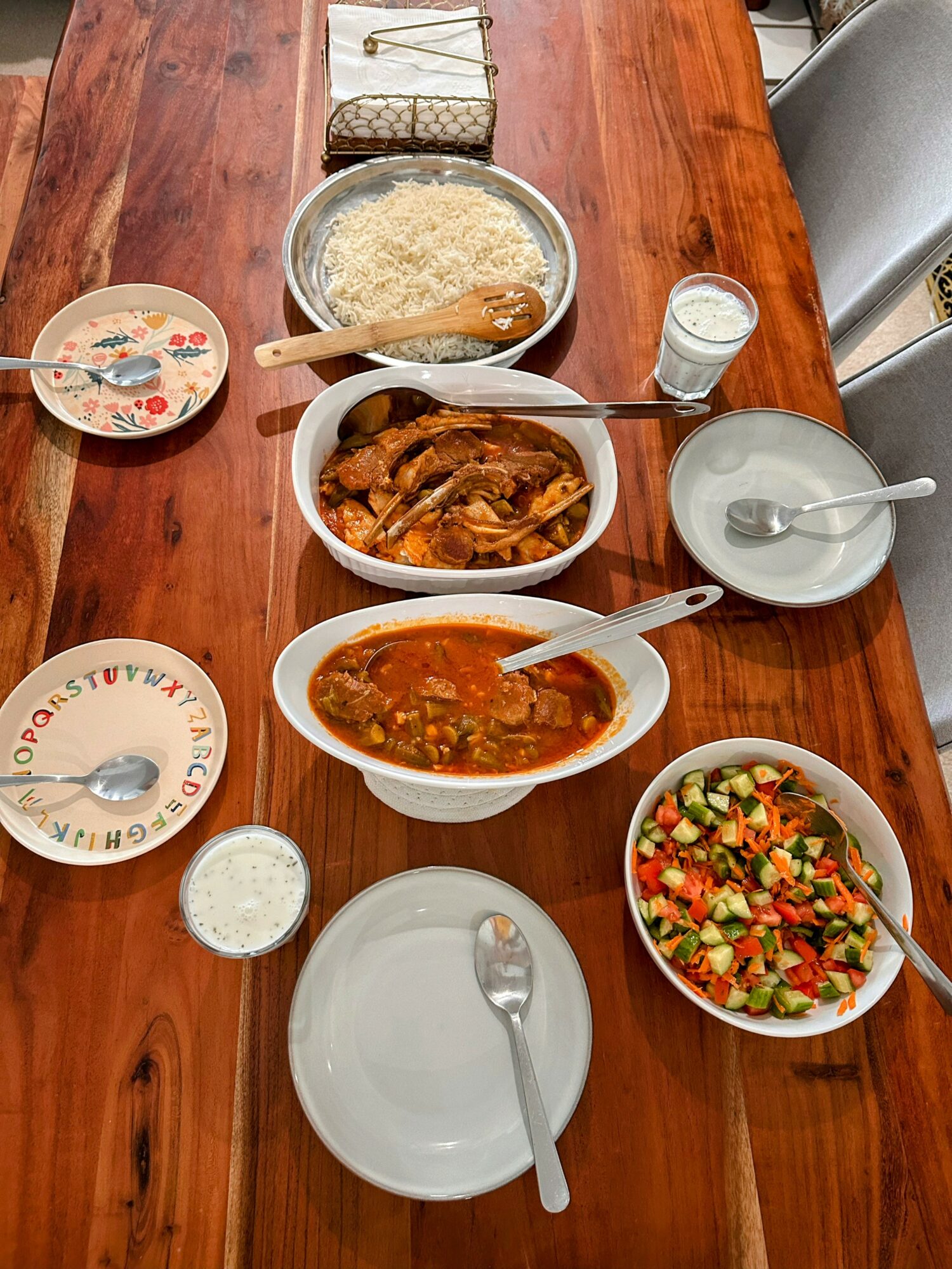 Table with rice, chicken stew, vegetable salad, and drinks, set for a meal.