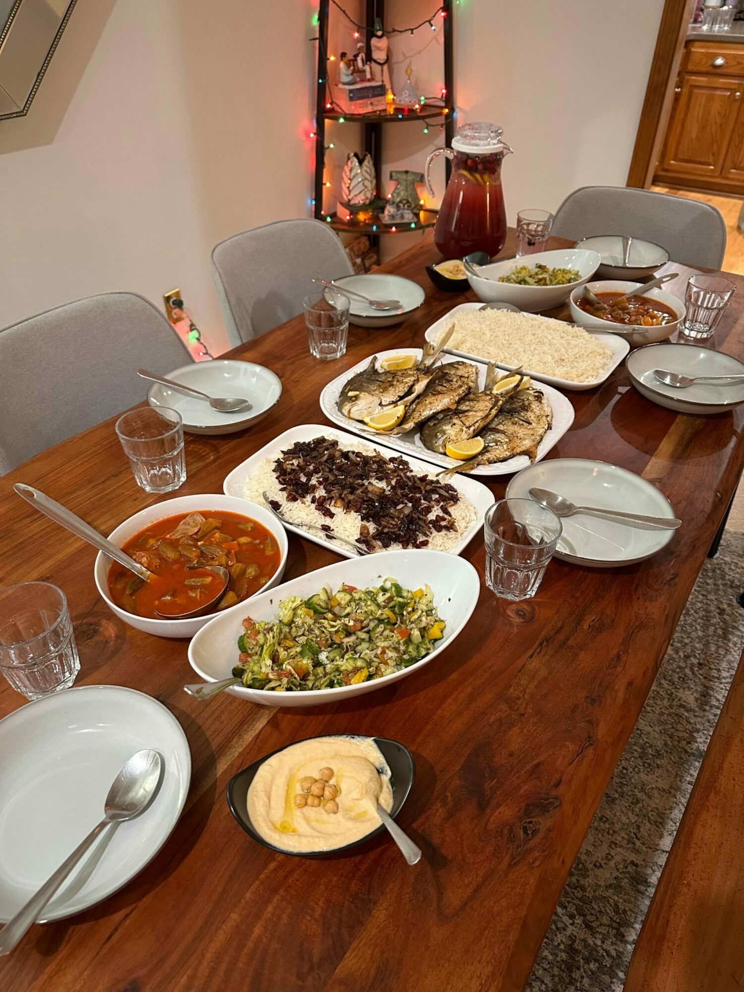 A table with various dishes including fried chicken, rice, vegetables, and soup, set with glasses and plates.