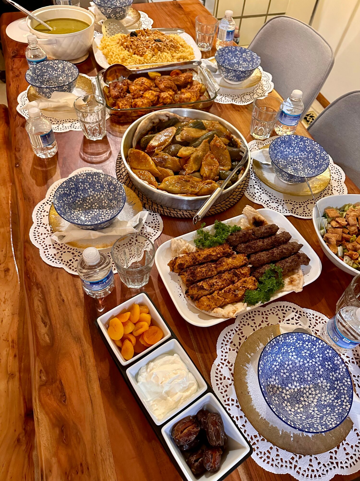 A table set with various dishes, bowls, and plates, including fried foods, vegetables, and sauces, with water bottles and decorative plates.