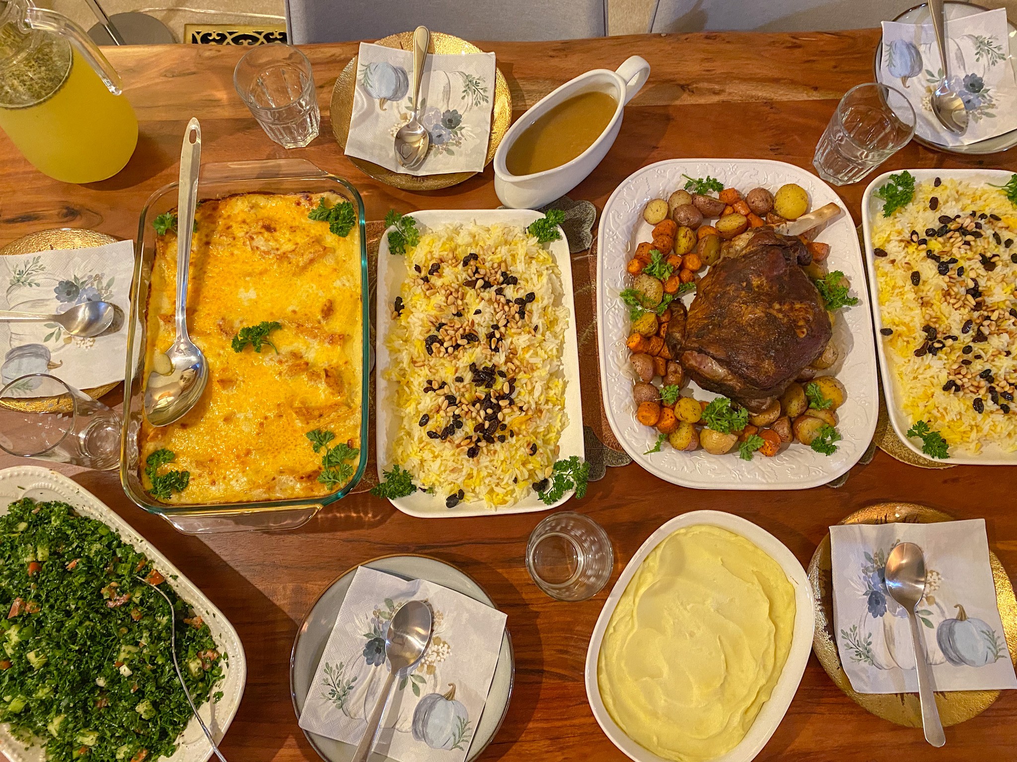 Table with various dishes including casseroles, a bowl of mashed potatoes, and drinks, set with napkins and utensils.