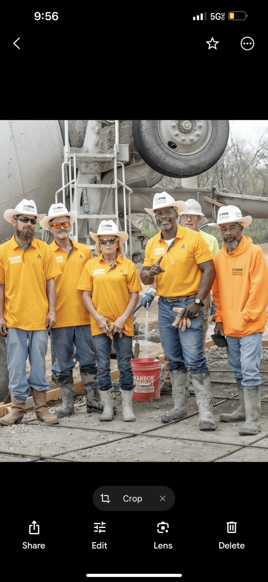 Group of six people wearing yellow and orange shirts, hats, and boots standing outdoors near equipment.