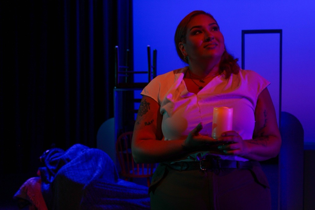 Woman sitting on a couch holding a glass, illuminated by blue and purple lighting, with a relaxed expression.