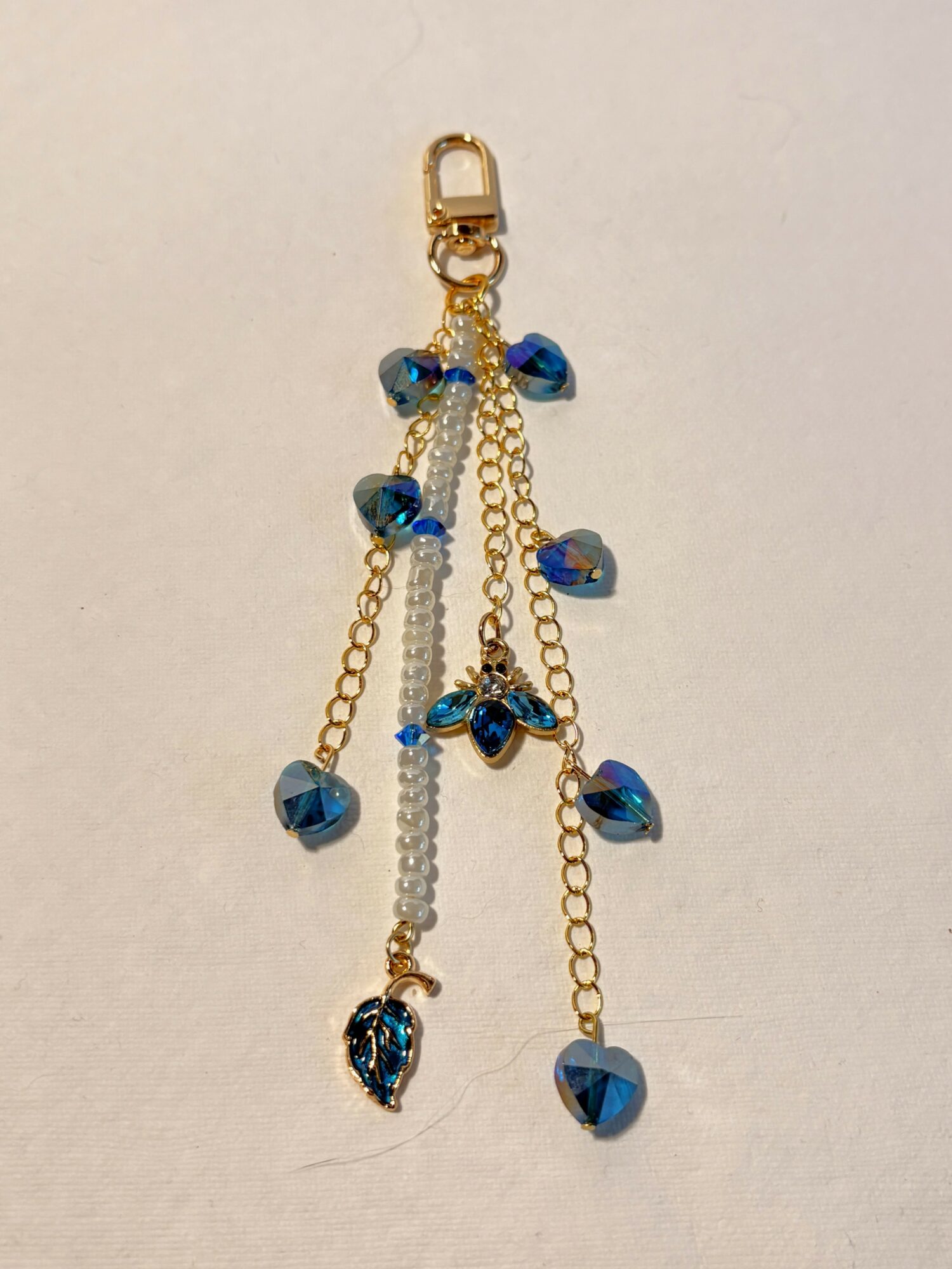 Gold chain with blue and clear beads, hanging from a clasp, on a plain background.