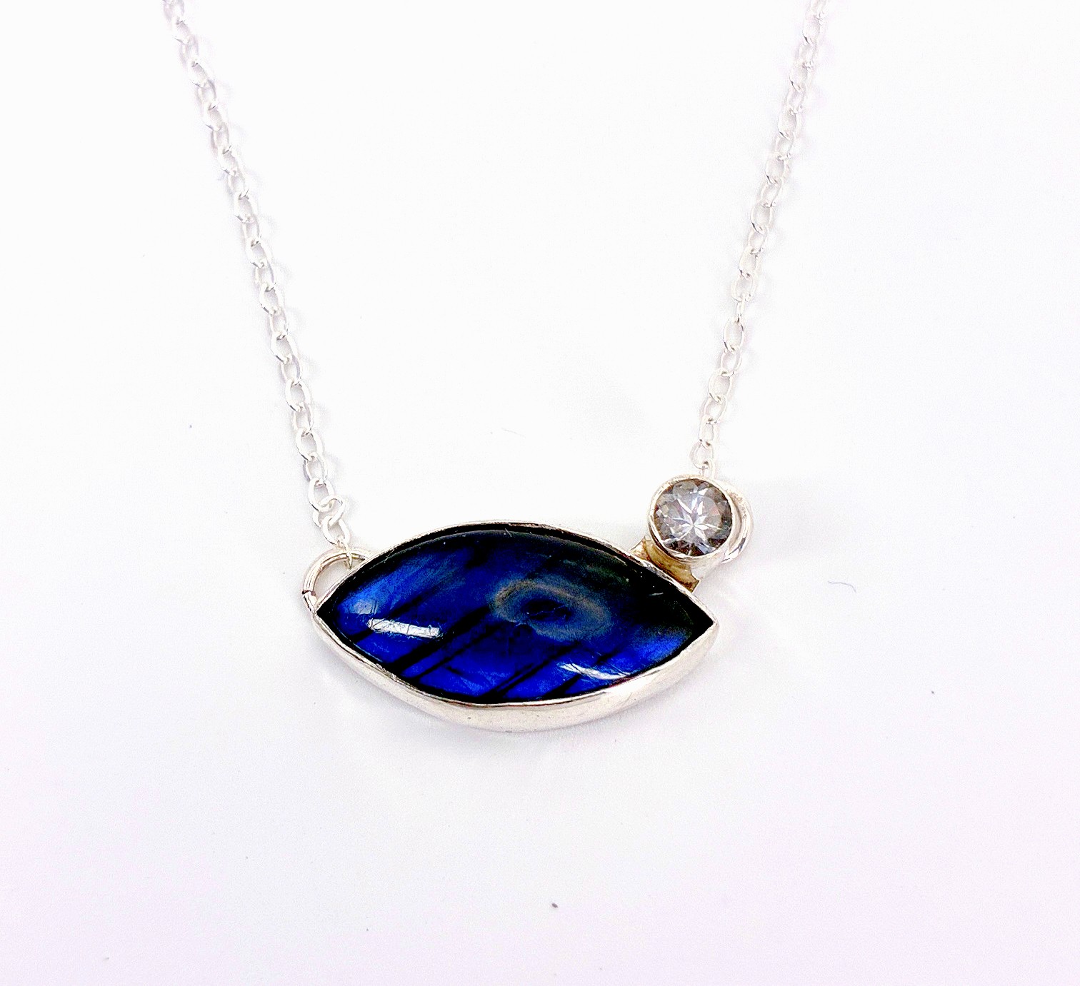 Silver necklace with a large blue oval gemstone and a small clear gemstone on a chain.