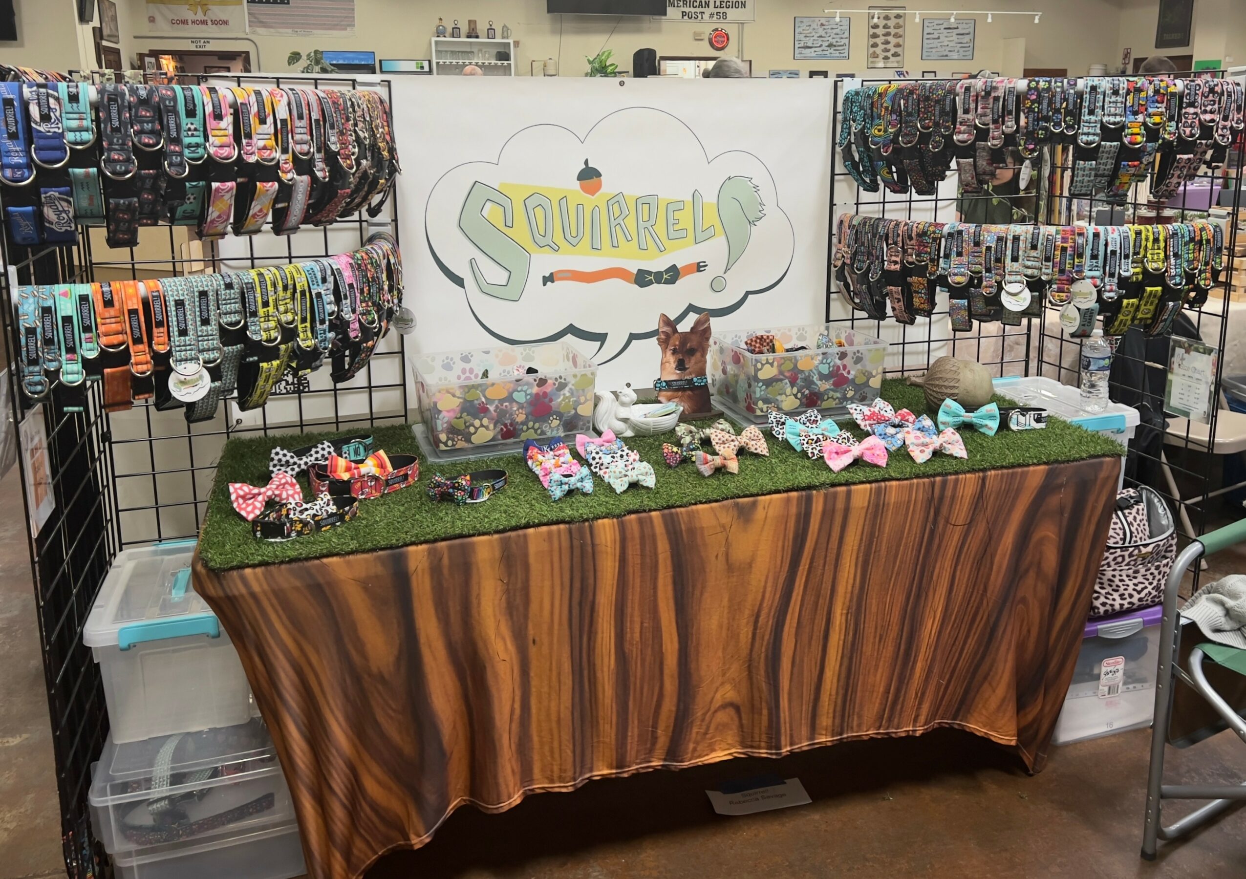 Display table with plush toys and accessories, sign reading 'Squirrel,' in a store with shelves of socks in background.