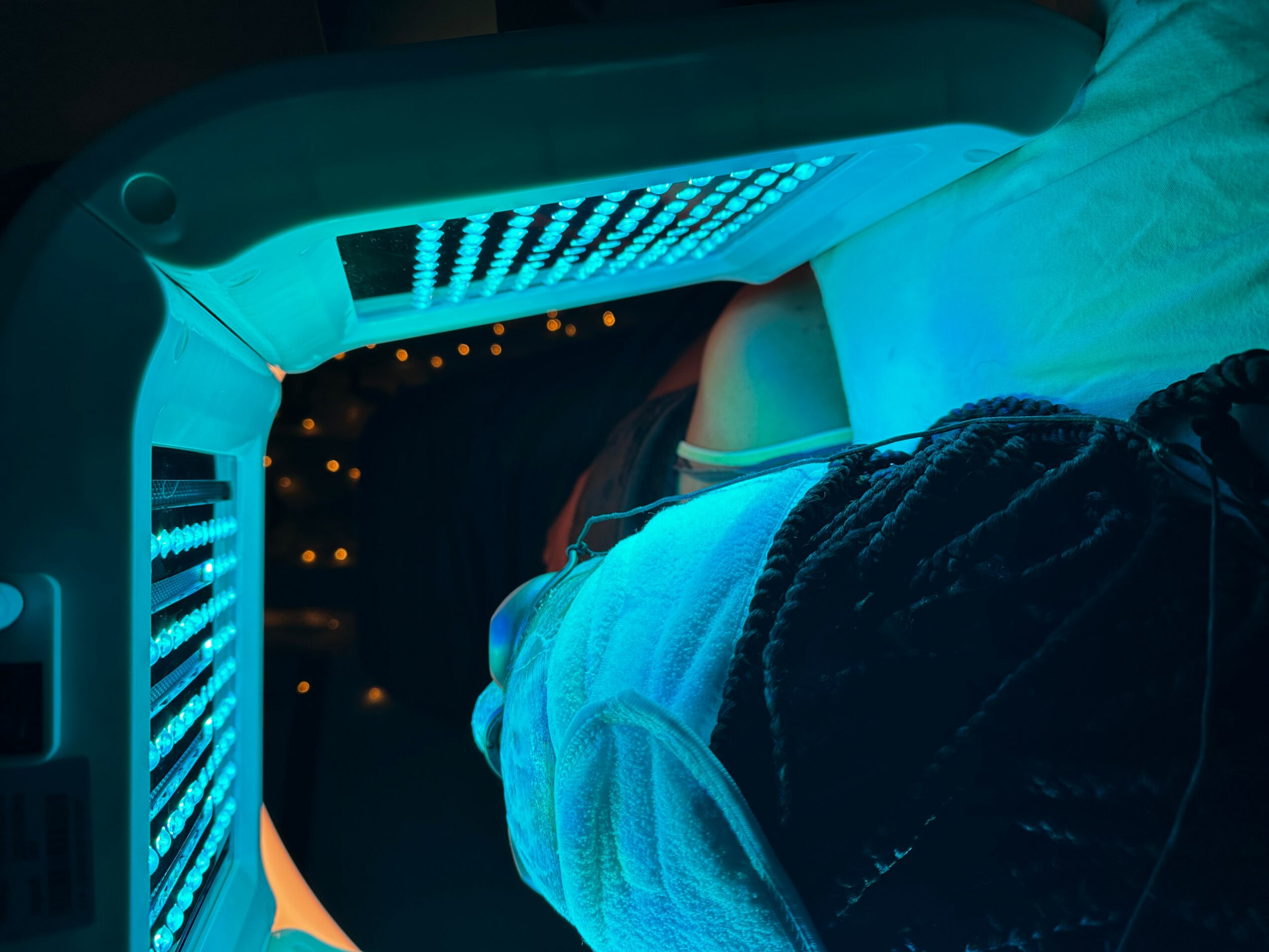 Person lying in a bed with a curved, illuminated medical device or monitor above them, showing blue and orange lights.