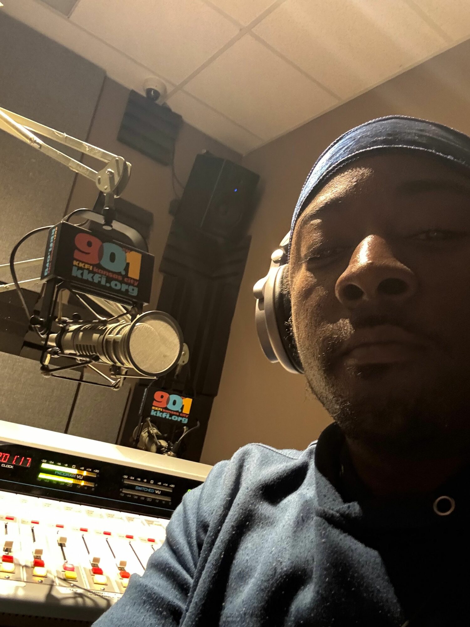 Person in a recording studio with a microphone and audio equipment, looking at the camera.