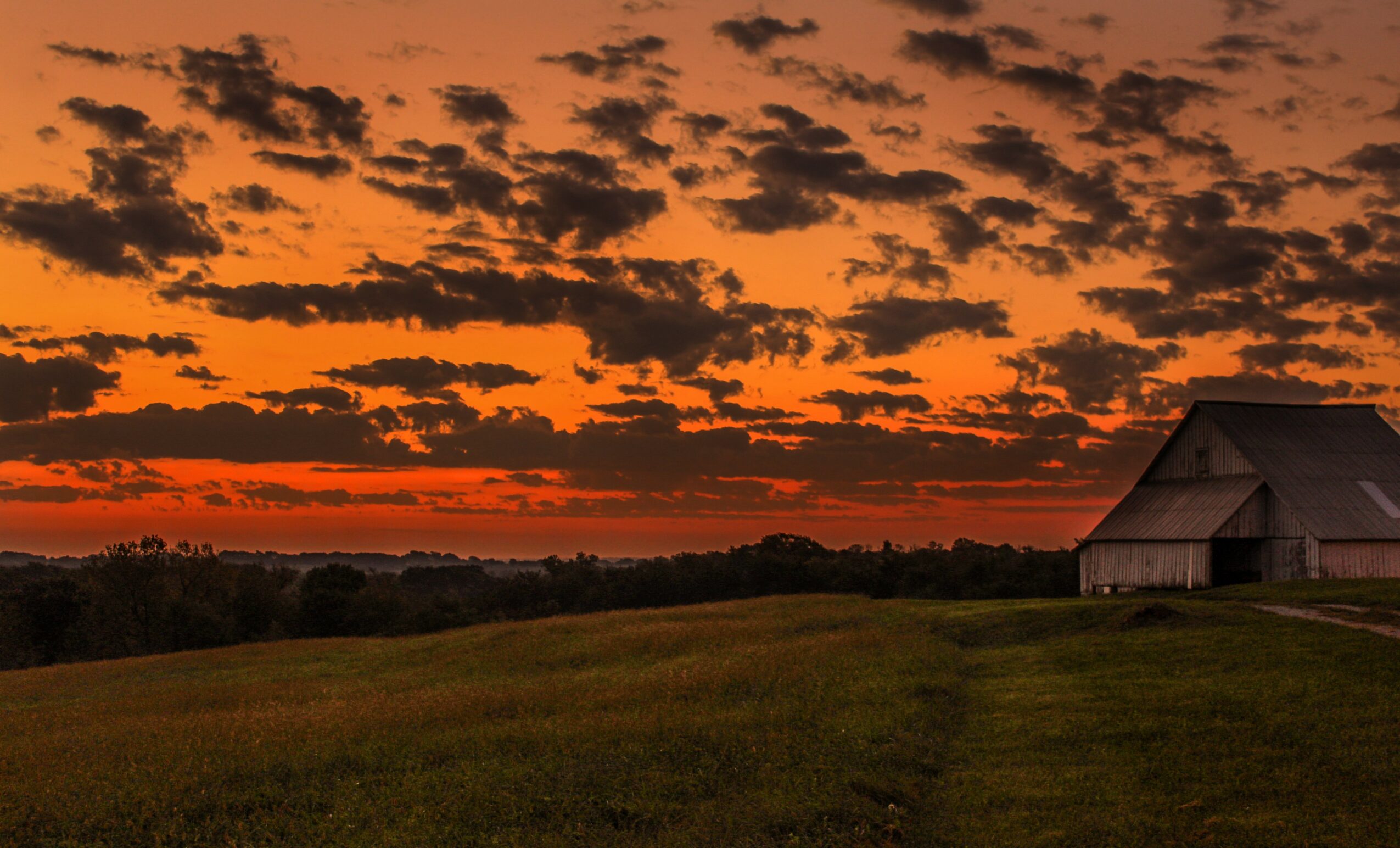 Sunset sky with orange and dark clouds over a grassy field and barn, landscape scene.