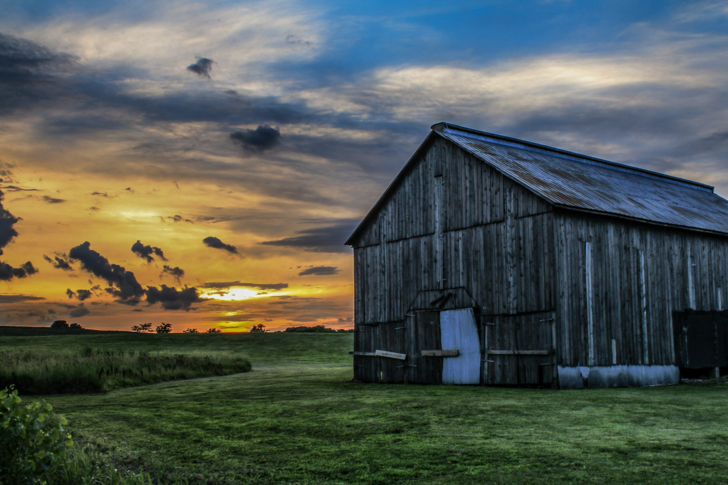 Barn on a grassy field during sunset with a colorful sky and clouds