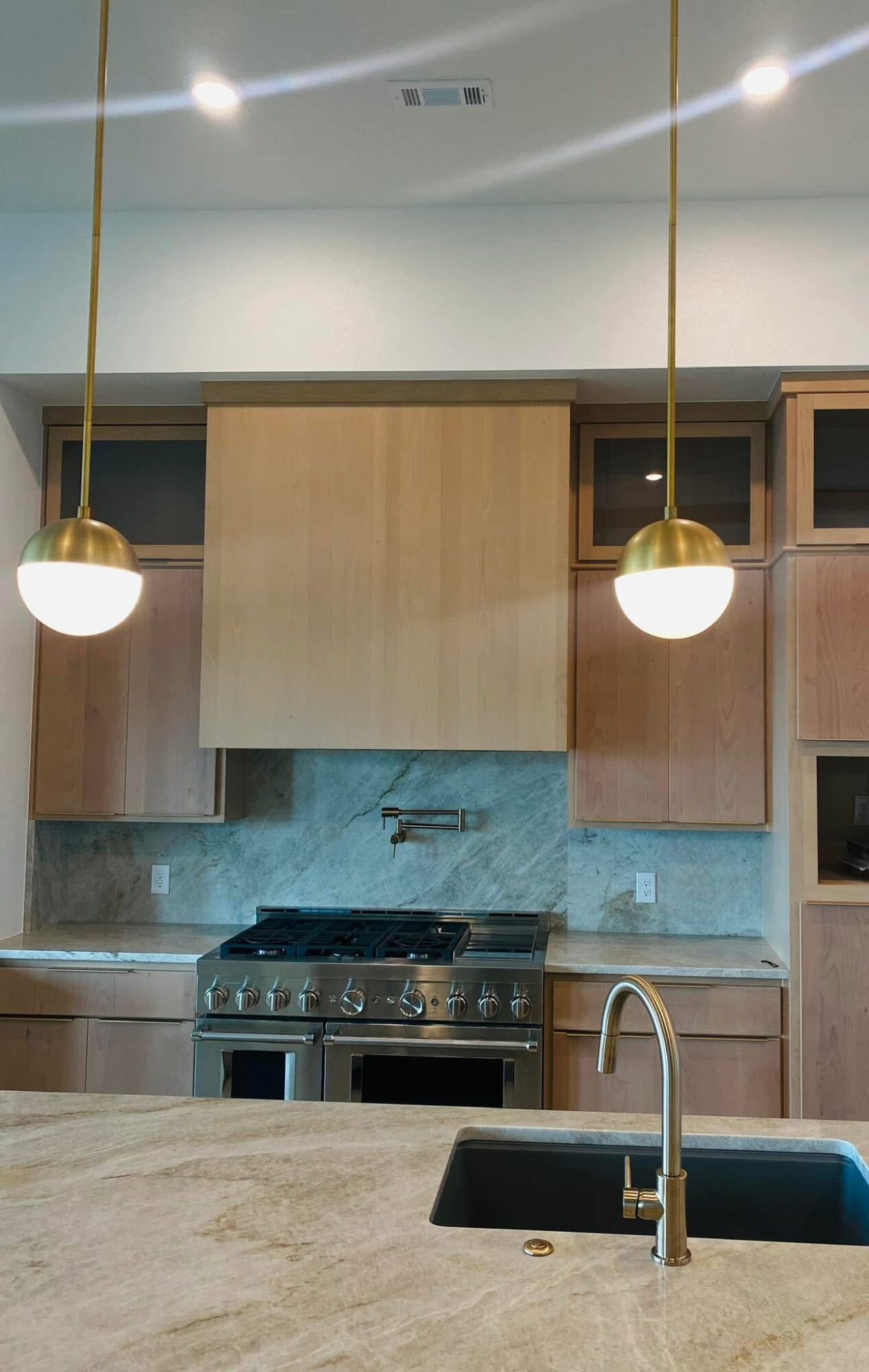 Kitchen with wooden cabinets, a stove, and two hanging pendant lights, viewed from a countertop with a sink.