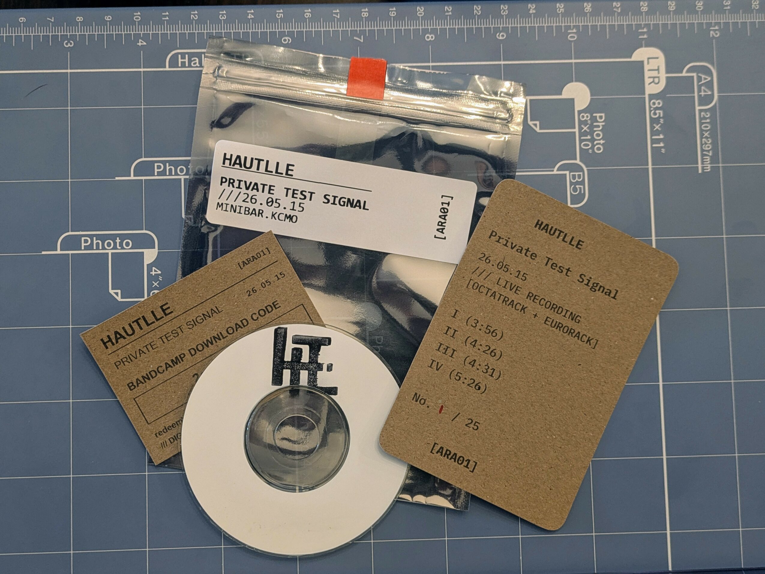Test signal device, two brown tags, and a white circular object on a blue cutting mat with measurement markings.