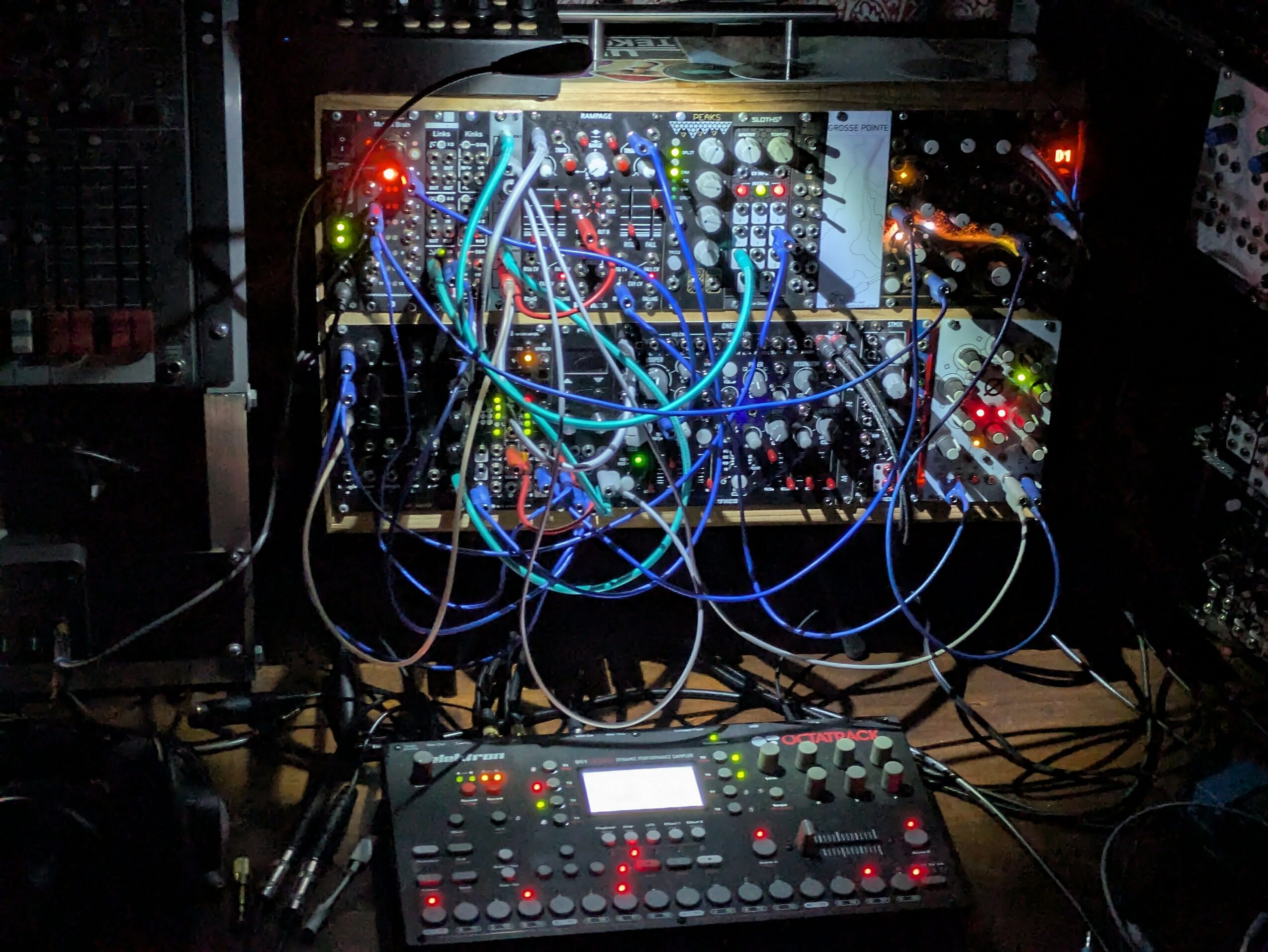 Electronic music equipment with cables, knobs, and screens in a dark setting.