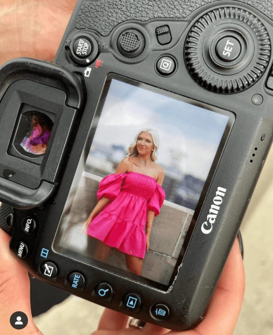 Camera screen shows a woman in a pink dress outdoors, with a cityscape in the background.