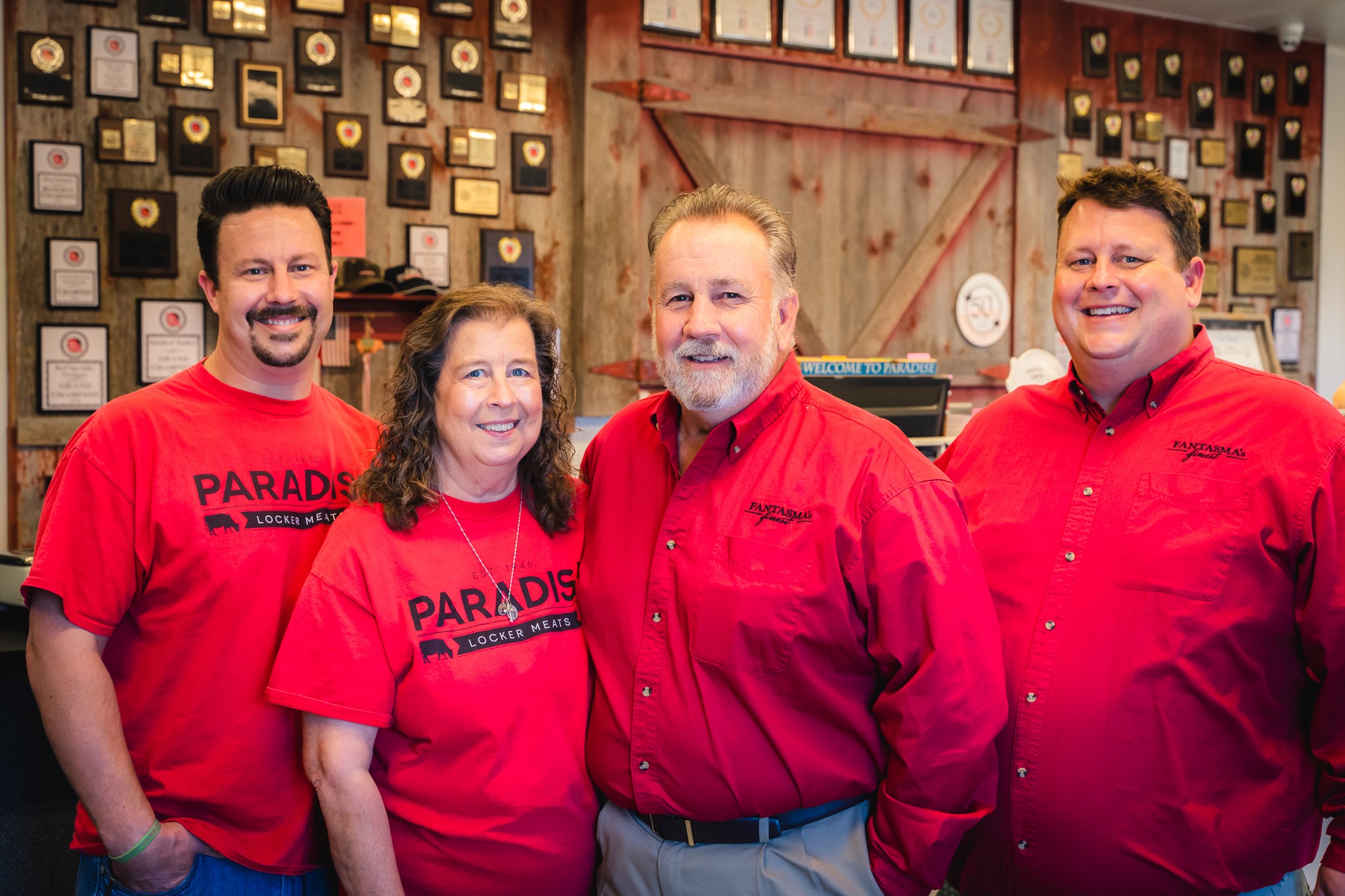 Four people wearing red shirts standing indoors, smiling, with a decorated wall behind them.
