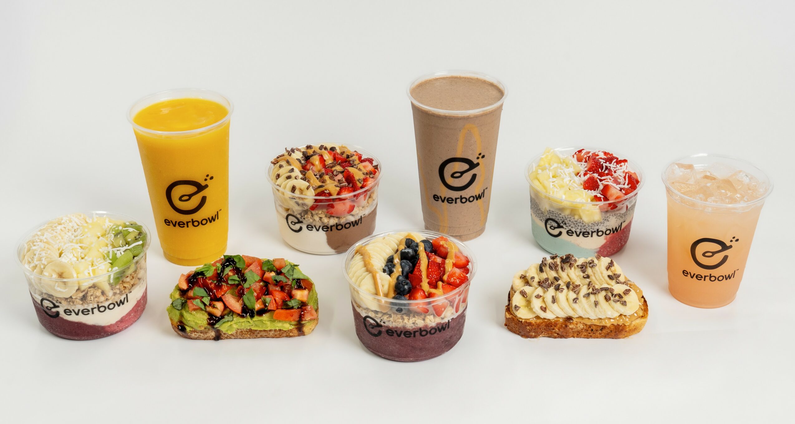 Assorted desserts and drinks on a white surface, including smoothies, cakes, and a slice of layered dessert.
