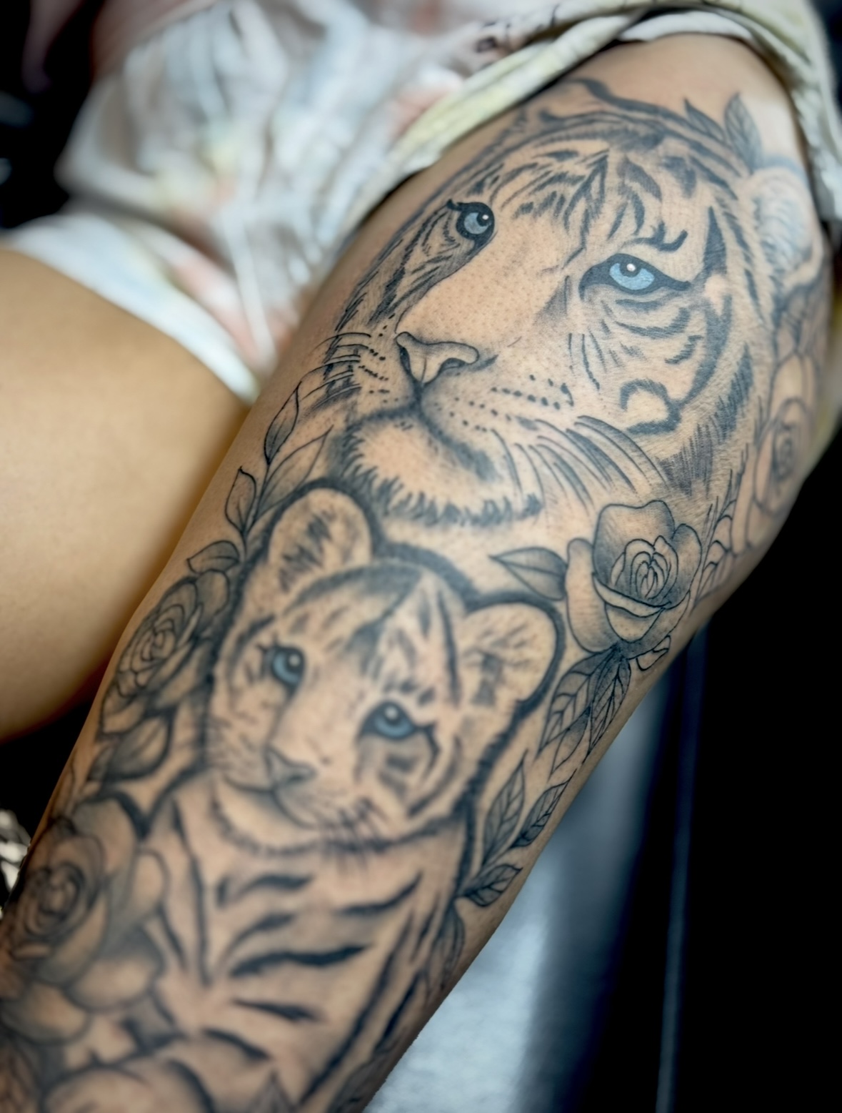 Tattoo of a tiger's face with detailed fur and eyes, surrounded by flowers on a person's arm.